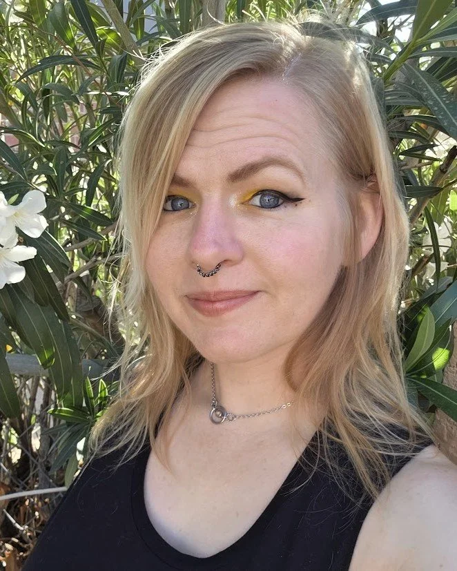 Mandy Thompson, LMHC, with a half smile to the camera. They are outdoors, in front of a flowering plant that fills the background.
