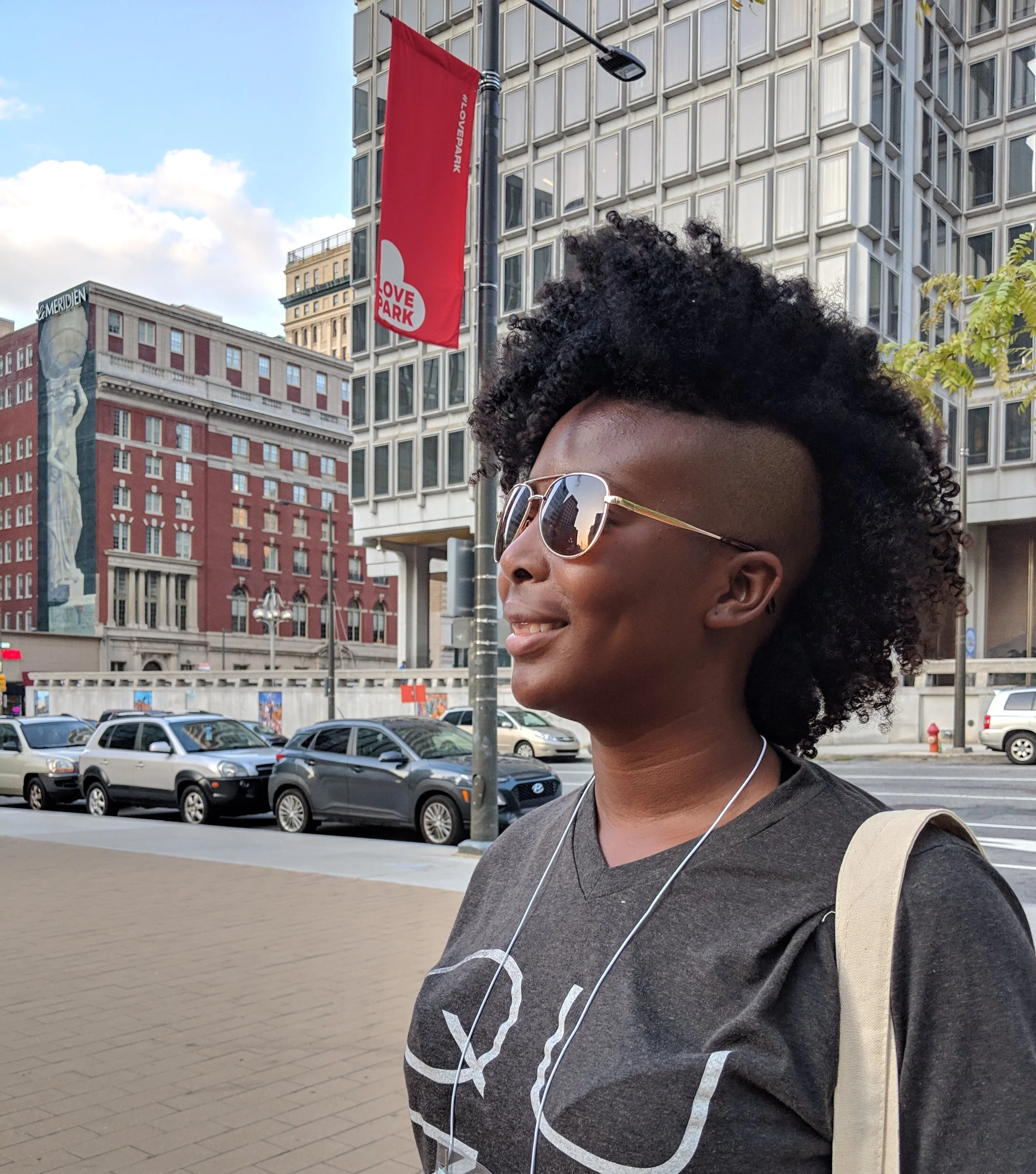 Rhamah Norris, LMHC, LMFT seen in three quarter profile in a city. They are wearing sunglasses and smiling off camera.