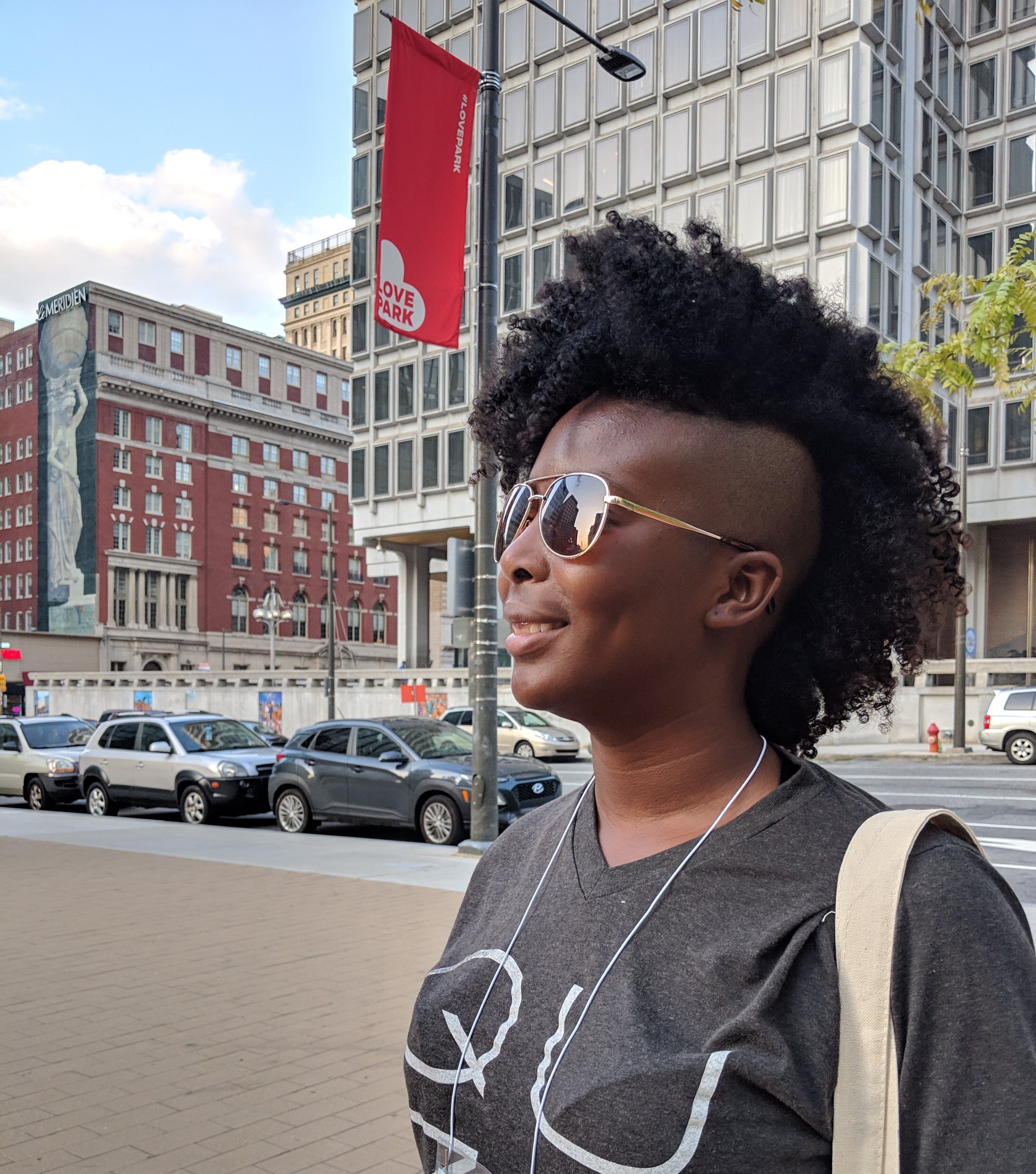 Rhamah Norris, LMHC, LMFT seen in three quarter profile in a city. They are wearing sunglasses and smiling off camera.