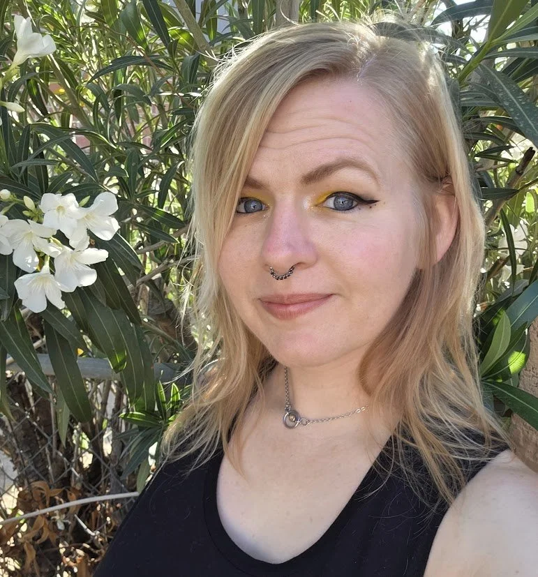 Mandy Thompson, LMHC, with a half smile to the camera. They are outdoors, in front of a flowering plant that fills the background.