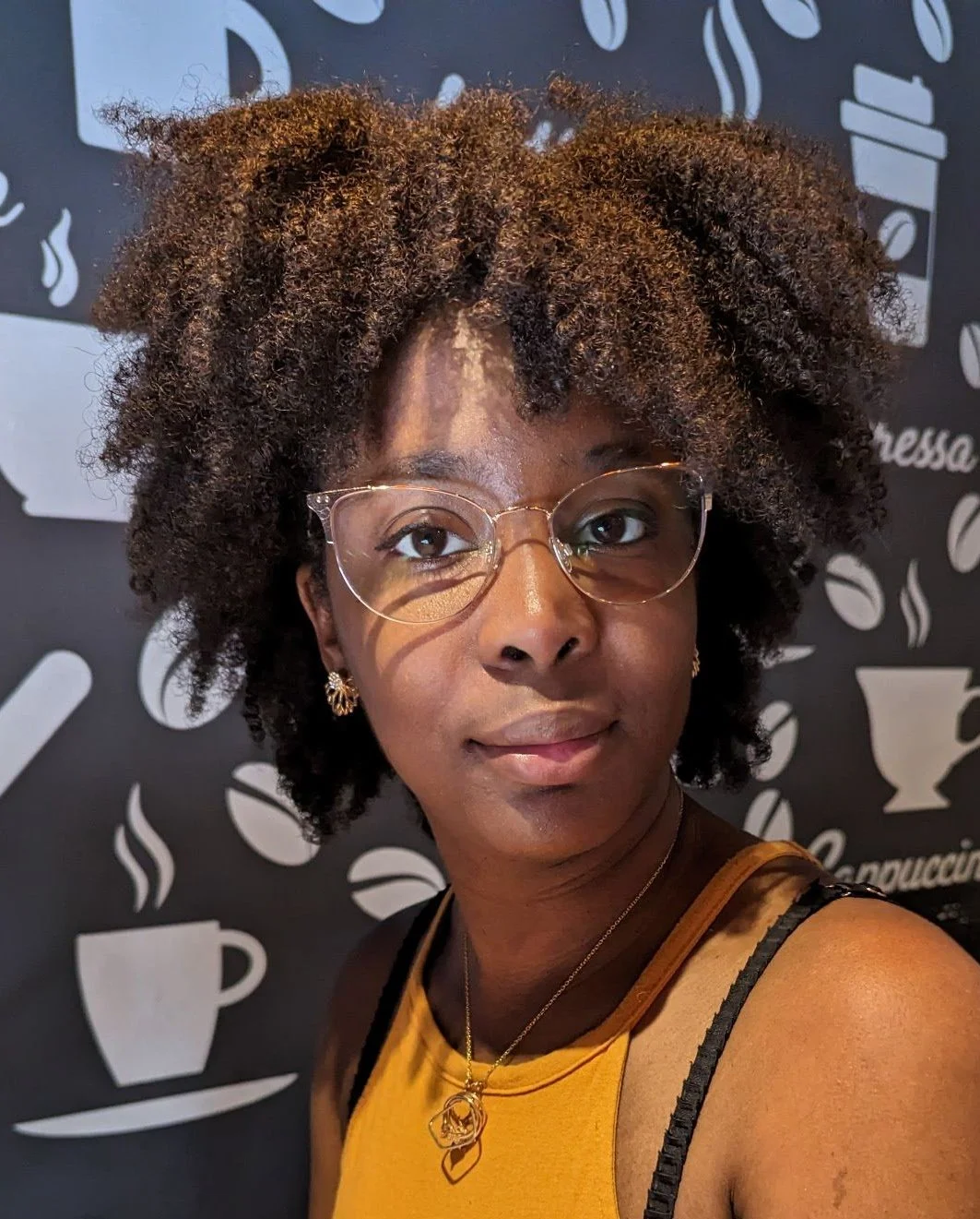 Rhamah Norris, LMFT, LMHC sitting in front of a wall with coffee graphics. She is looking directly at the camera with a half-smile.