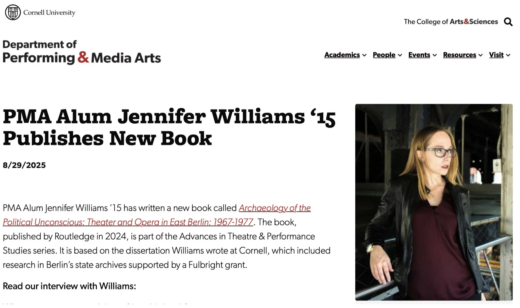 Cornell University announcement: PMA Alum Jennifer Williams '15 Publishes New Book. A woman with red hair and glasses wearing a black jacket and maroon top, standing outdoors in an industrial setting with metal structures in the background.