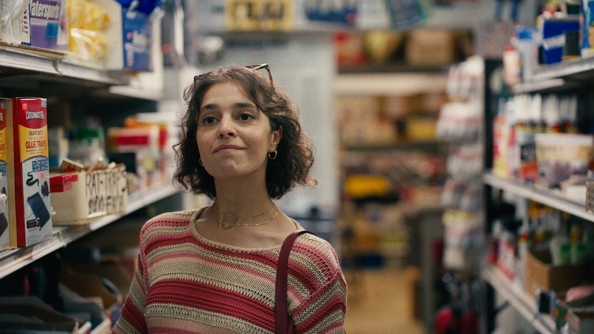 Young woman with brown curly hair wearing a red and beige striped sweater, shopping in a grocery store aisle.