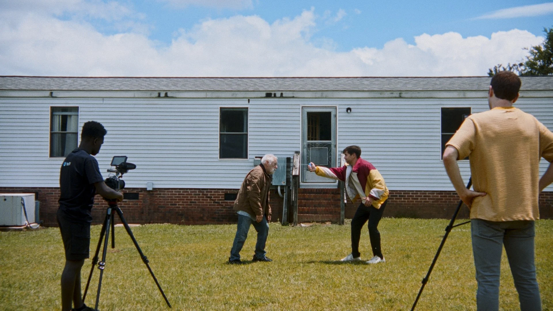 Group of young people filming a scene outdoors in a grassy yard, with a white house in the background.