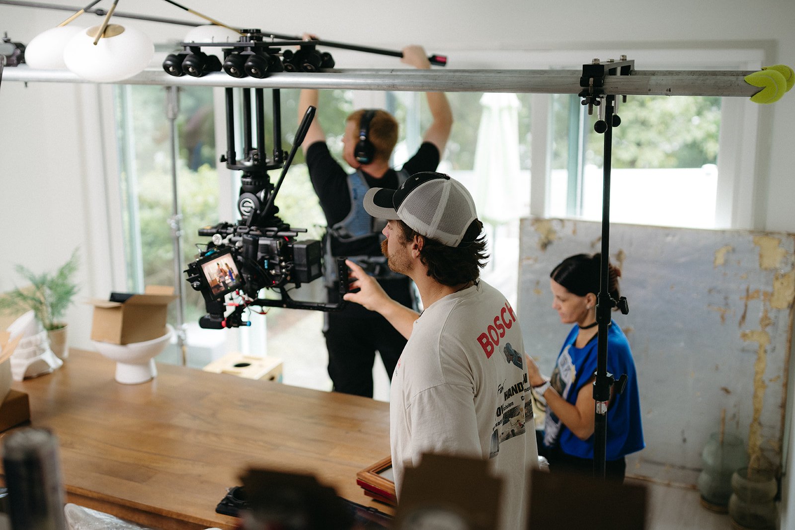 Filming crew setting up camera equipment indoors, with crew members wearing headphones and one person working on a tablet near a wooden table.