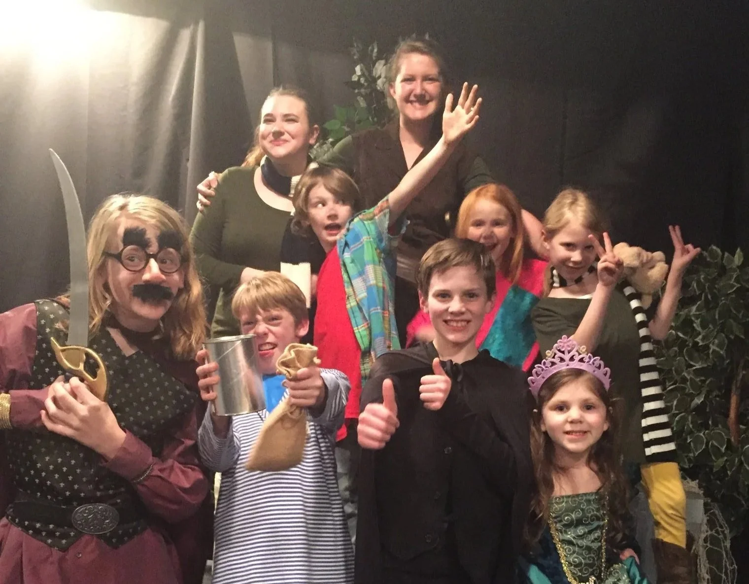 Group of children and adults dressed in costumes, smiling and posing together at a party or event.