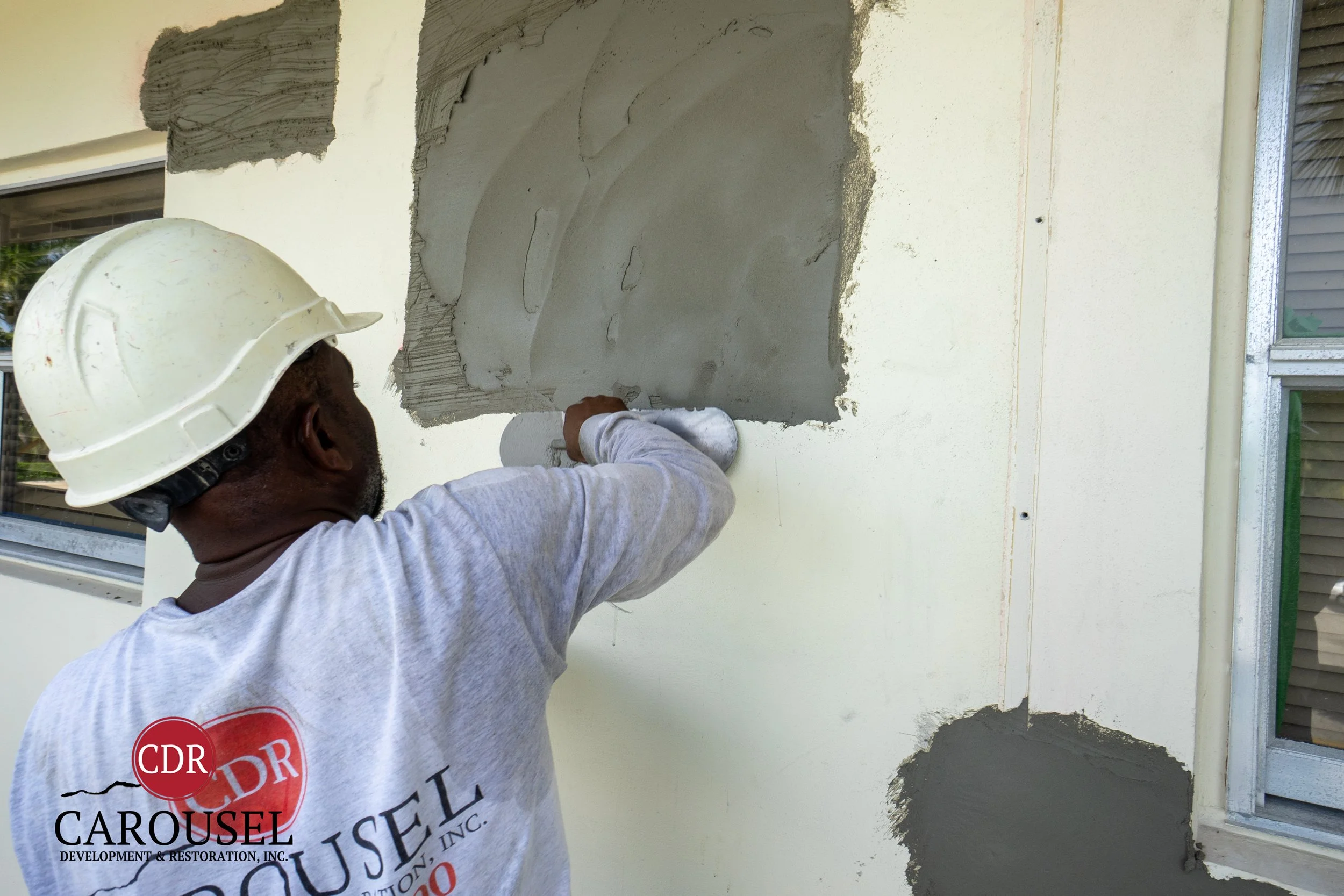 Carousel employee repairs stucco on the side of a building