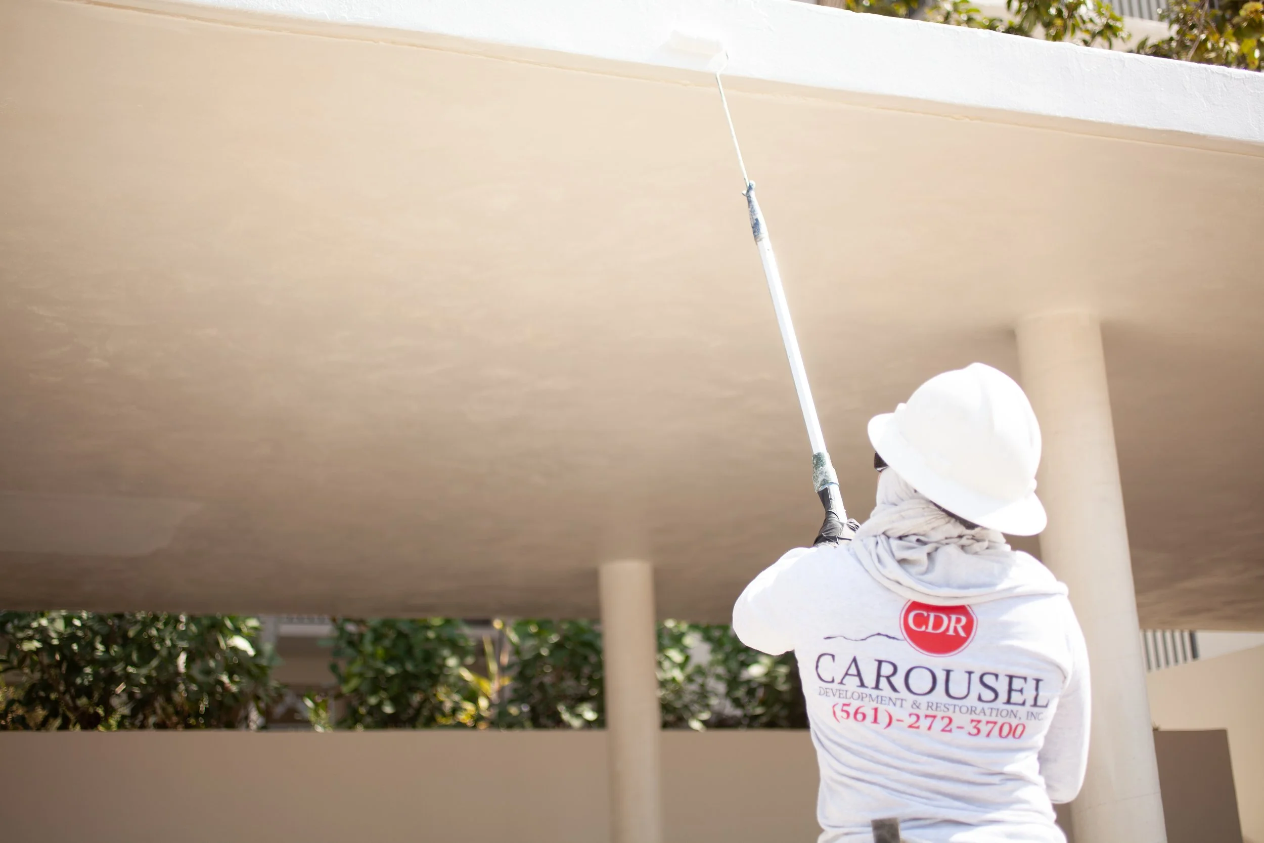 The back of Carousel employee painting exterior flat roof with a roller
