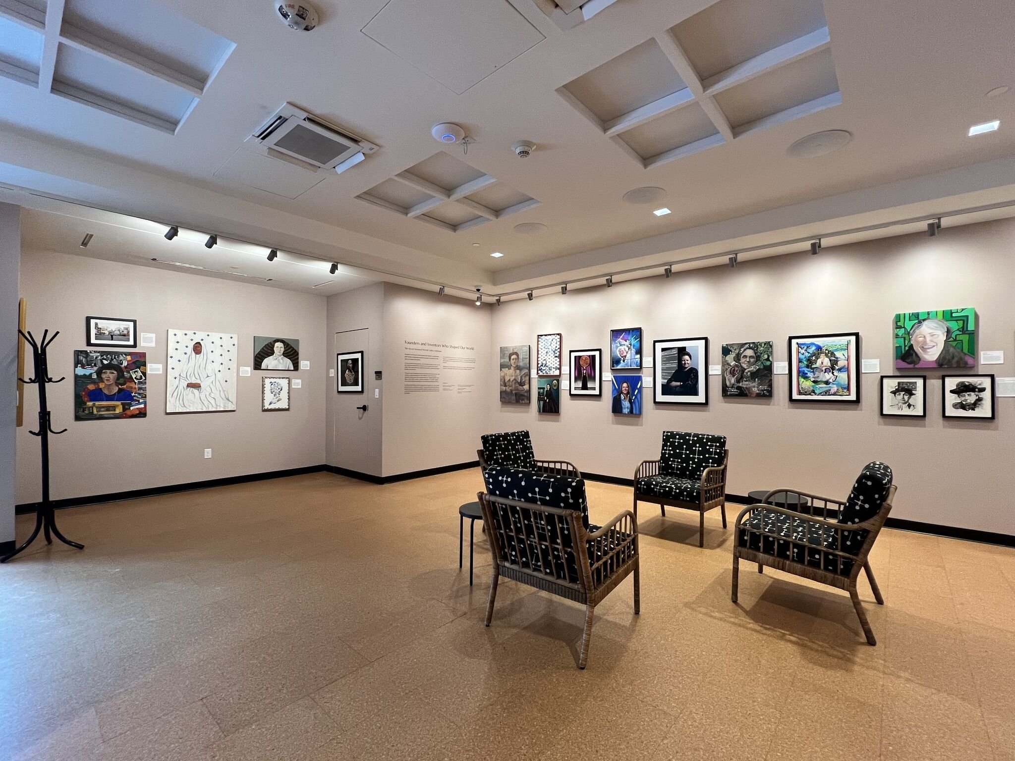The gallery space at The Alcove in Providence, Rhode Island, featuring the inaugural Portrait Gallery exhibition. Framed artworks in diverse styles line the warm beige walls, celebrating women and gender expansive people.