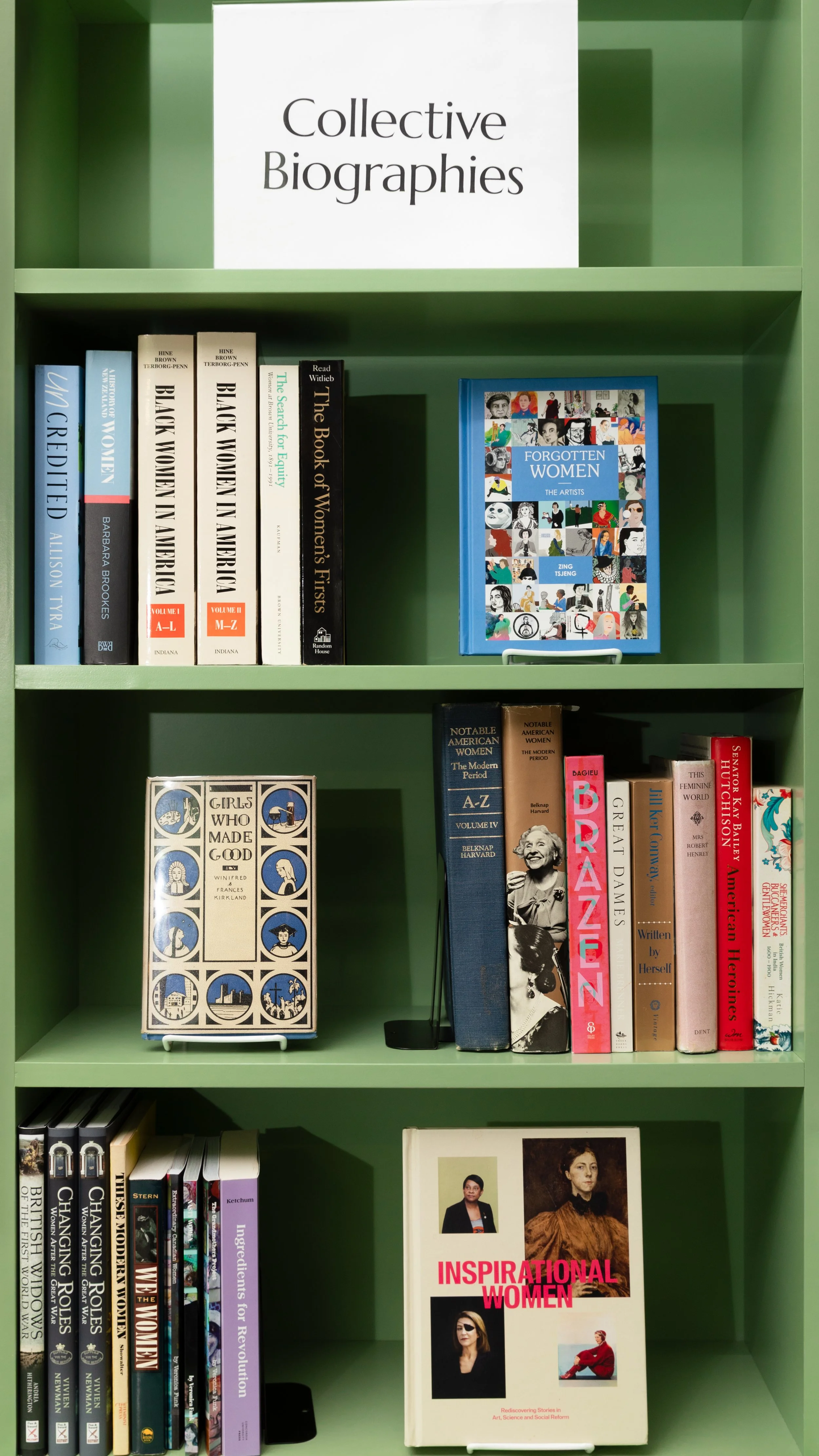 A curated green bookshelf filled with books celebrating women and gender expansive people at The Alcove Biographical Library, a feminist library in Providence, RI