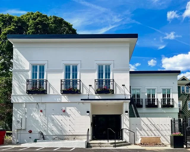 A photo of The Alcove building that is white with decorative details including black iron balconies.