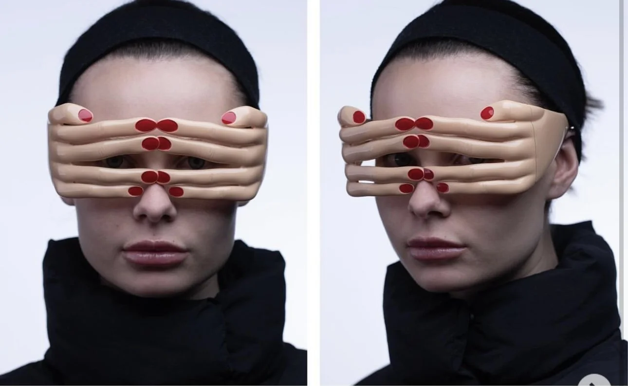 A person with a black headband and black clothing, holding a sculpture of multiple human hands with red nail polish over their eyes, creating an artistic visual. The image appears twice, showing different angles of the person.