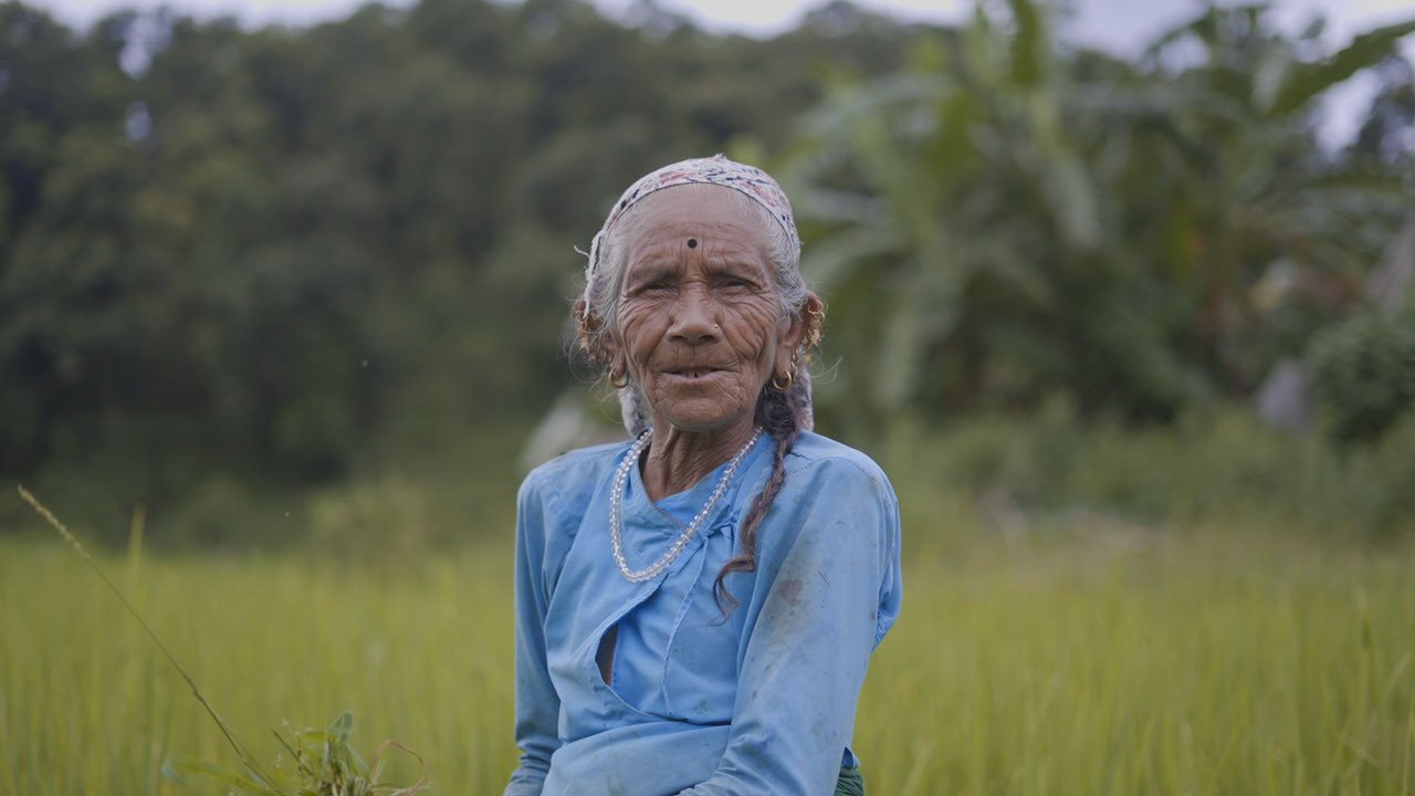 Two women outdoors with mountains and trees in the background. One woman is holding a tray and the other woman is serving herself food.