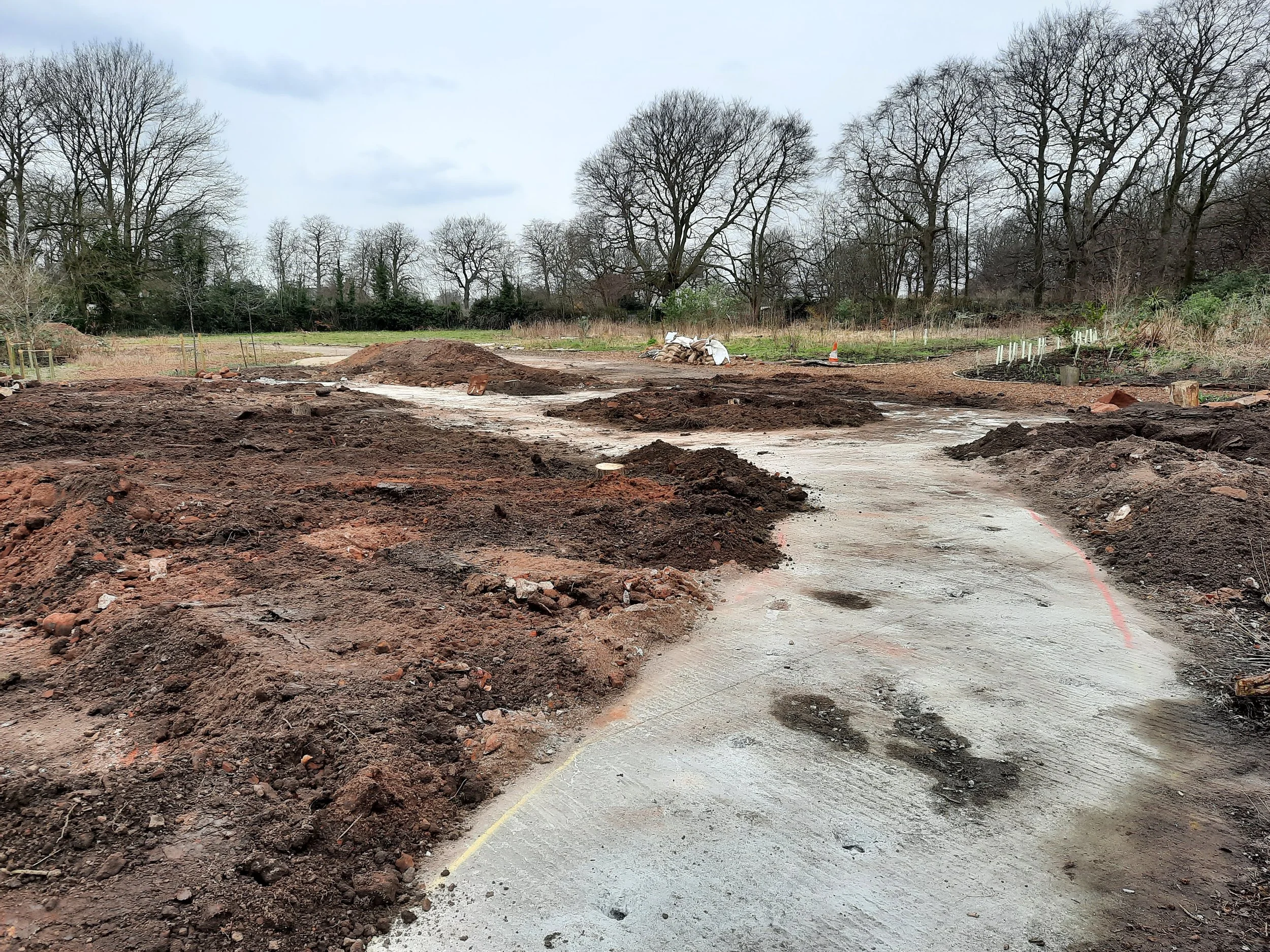 Construction site with a partially built path, dirt piles, and sparse trees in the background.