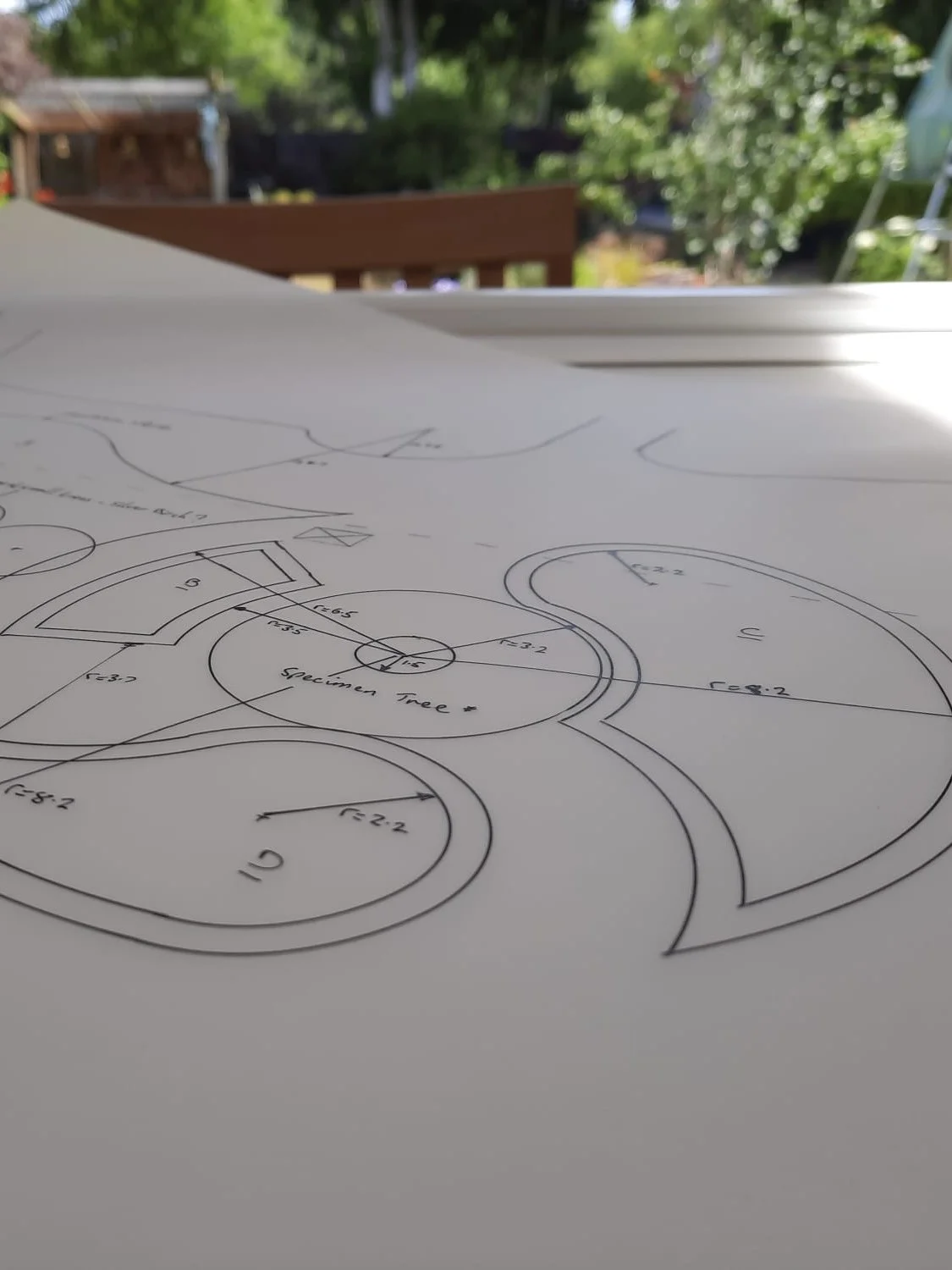 Technical drawing or plan with circles, measurements, and annotations on a white sheet of paper outdoors.