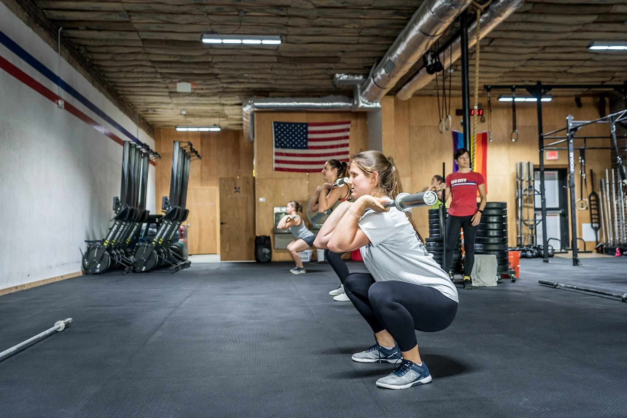 Women performing squats with barbells in a gym.