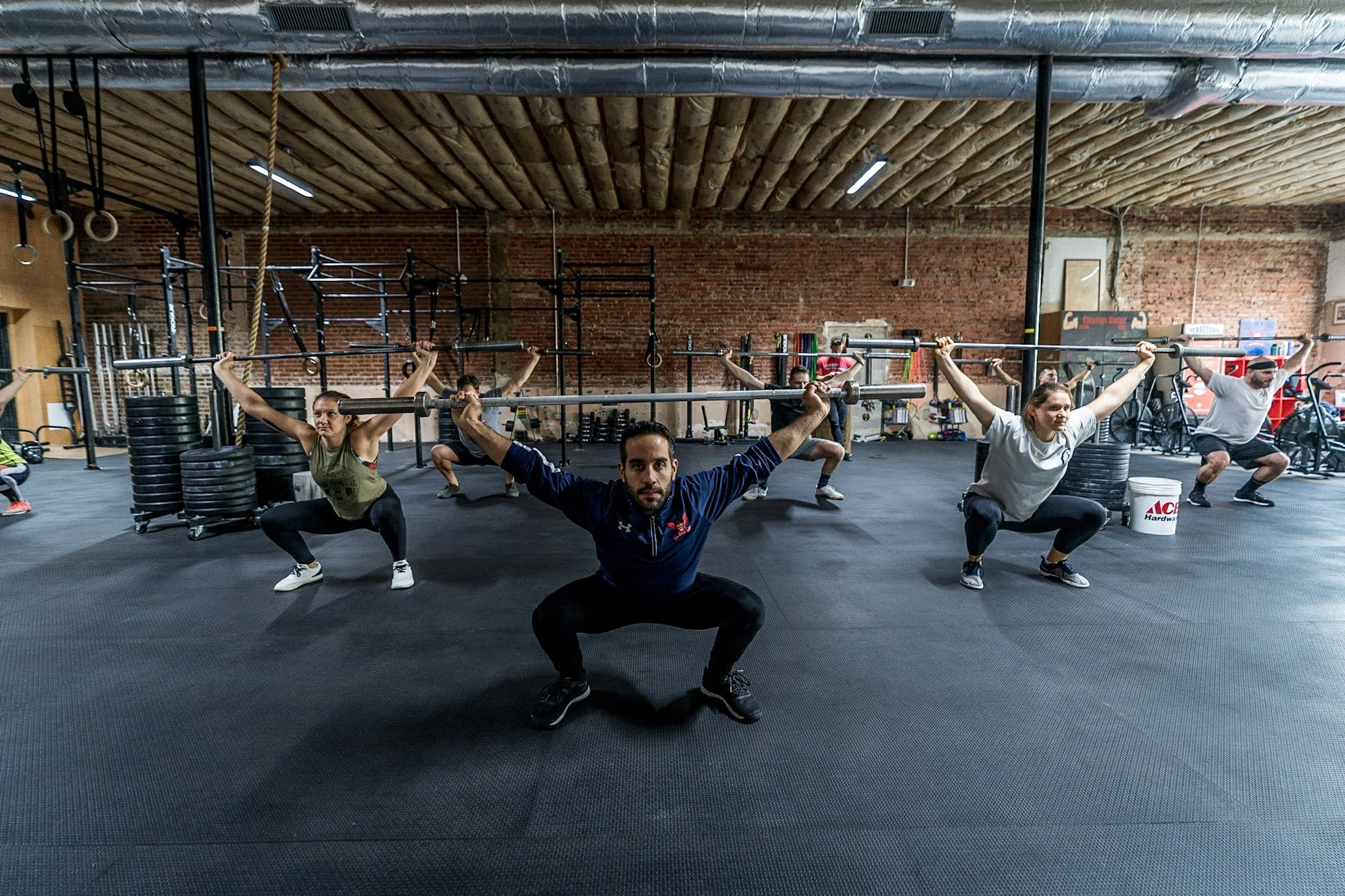 Group of people performing squats with barbells in a gym.