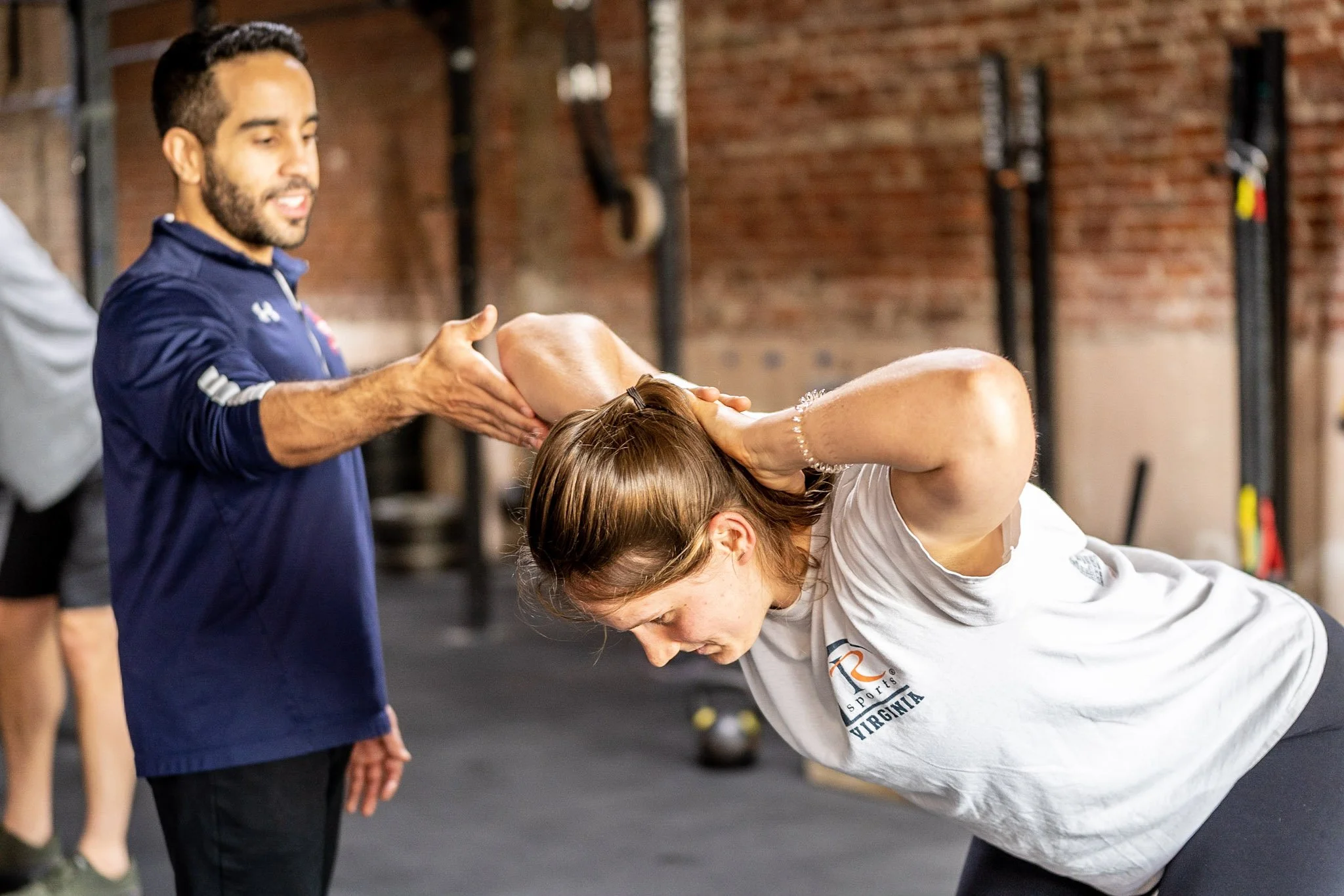 Personal trainer assisting woman with shoulder stretch at gym.