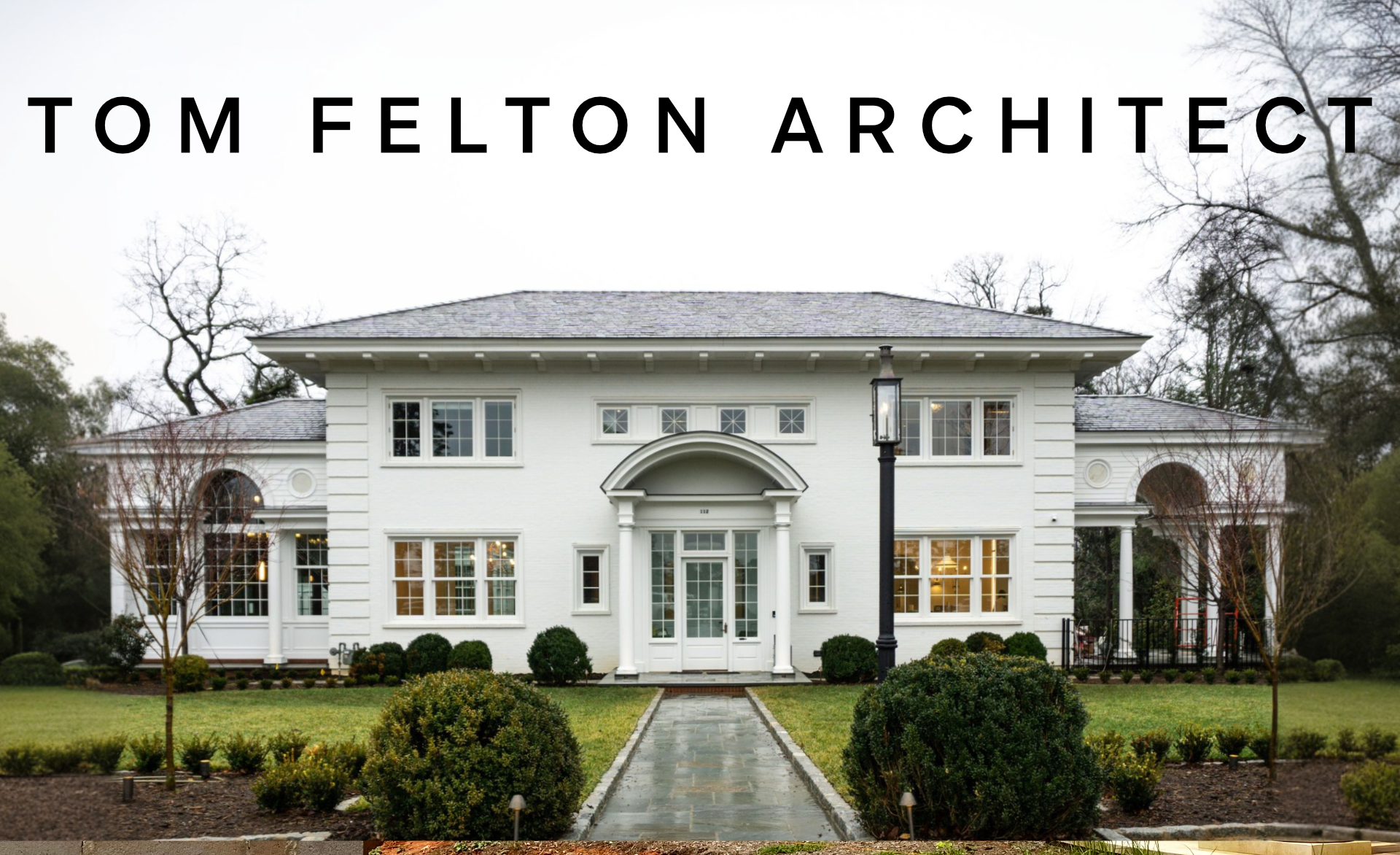 Front view of a large white residential house with landscaped front yard, trees, a pathway, and a black street lamp.