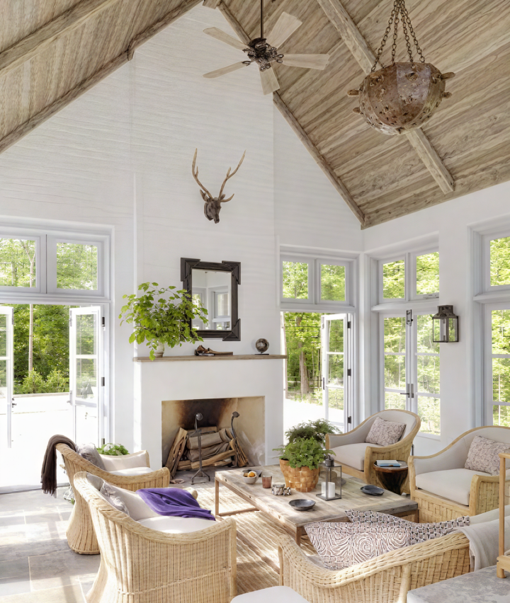 Bright living room with a high, wood-paneled ceiling, windows, and a stone fireplace. Decor includes an antler mount, and cream colored couches.