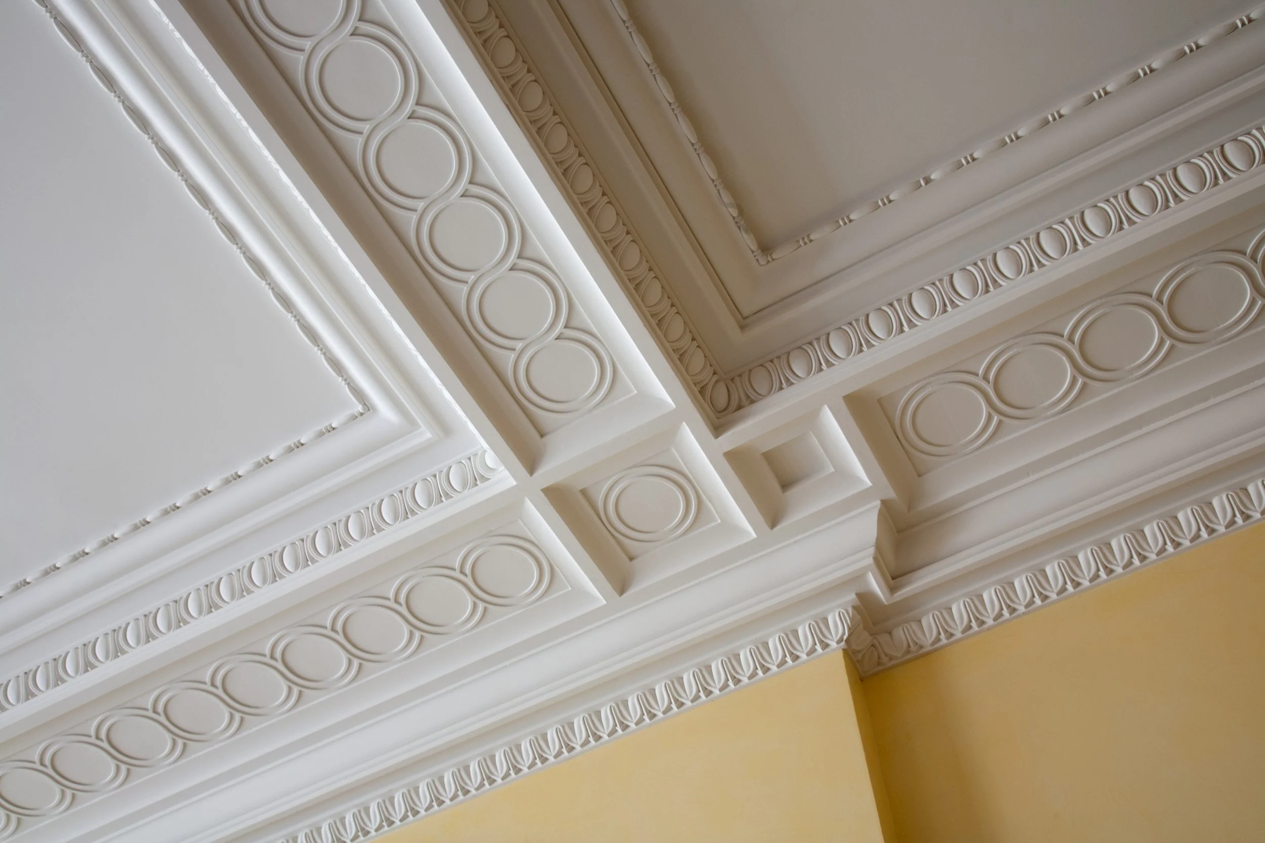 Ceiling molding with decorative circular and square patterns in a room with white and beige walls.