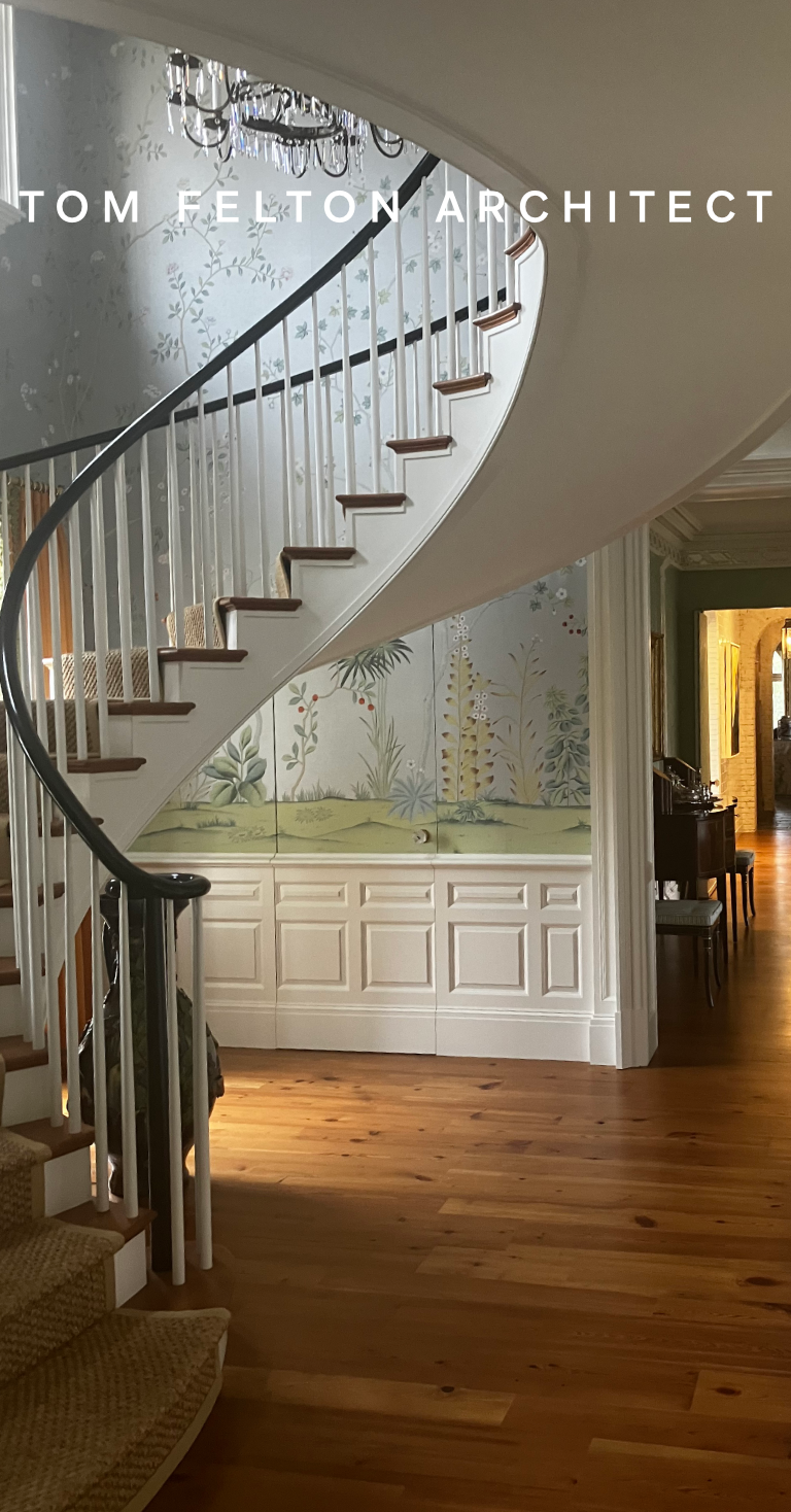 Interior view of a house featuring a curved staircase with white spindles and dark wood handrail, hardwood floors, painted wallpaper with botanical designs, and a chandelier hanging from the ceiling.