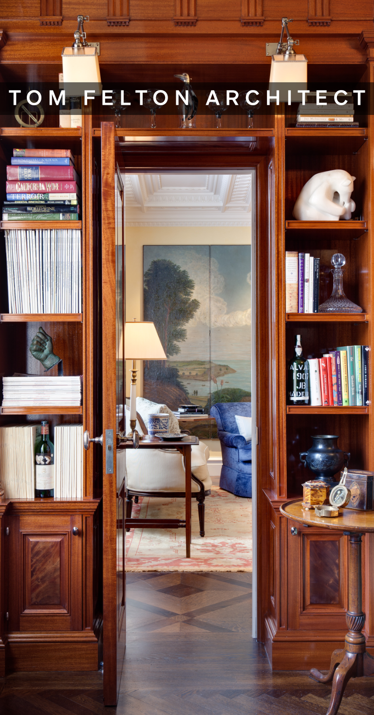 View through a wooden doorway into a cozy living room with a large landscape painting, a table lamp, and various furniture and decorative items.