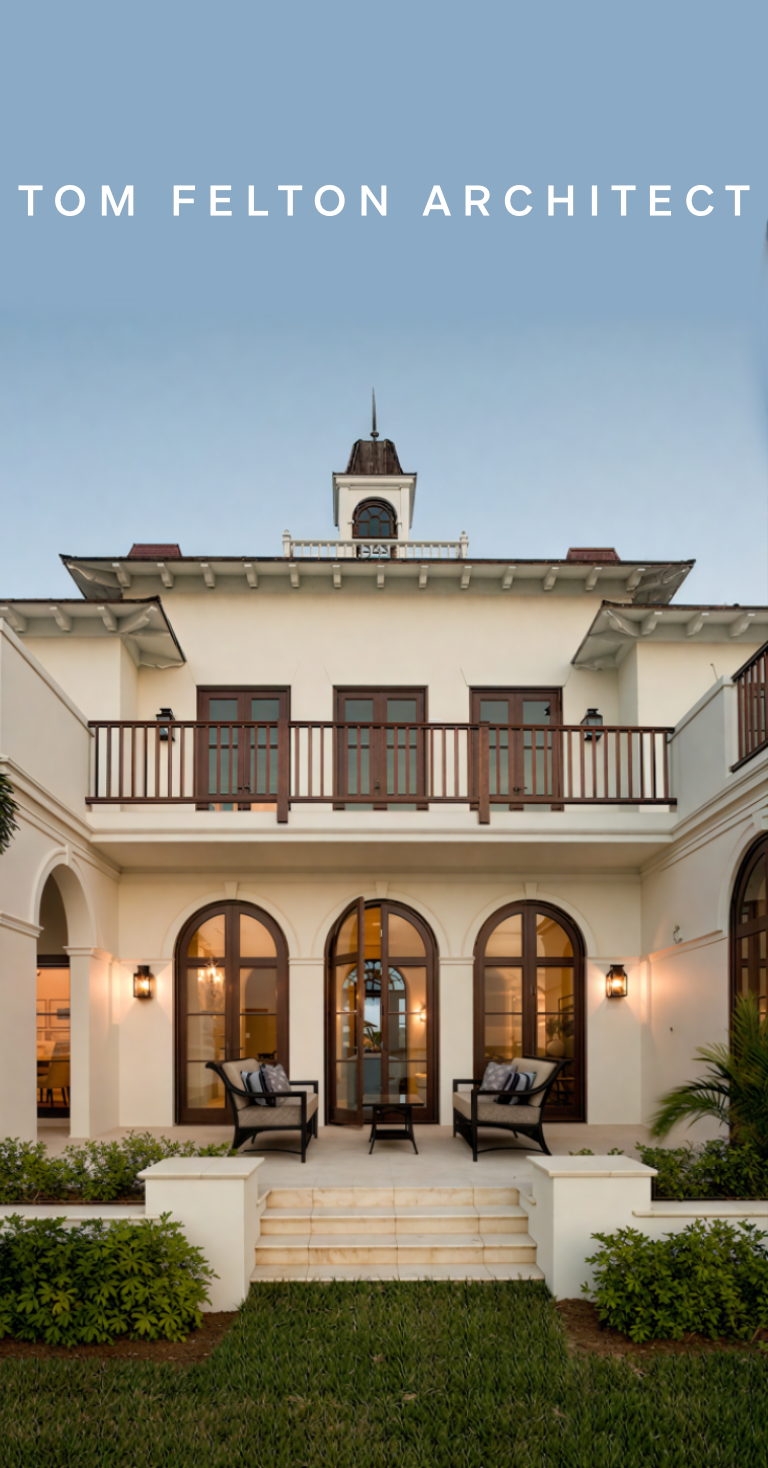 Exterior of a multi-story house with arched windows, a balcony, and a courtyard with chairs and greenery.