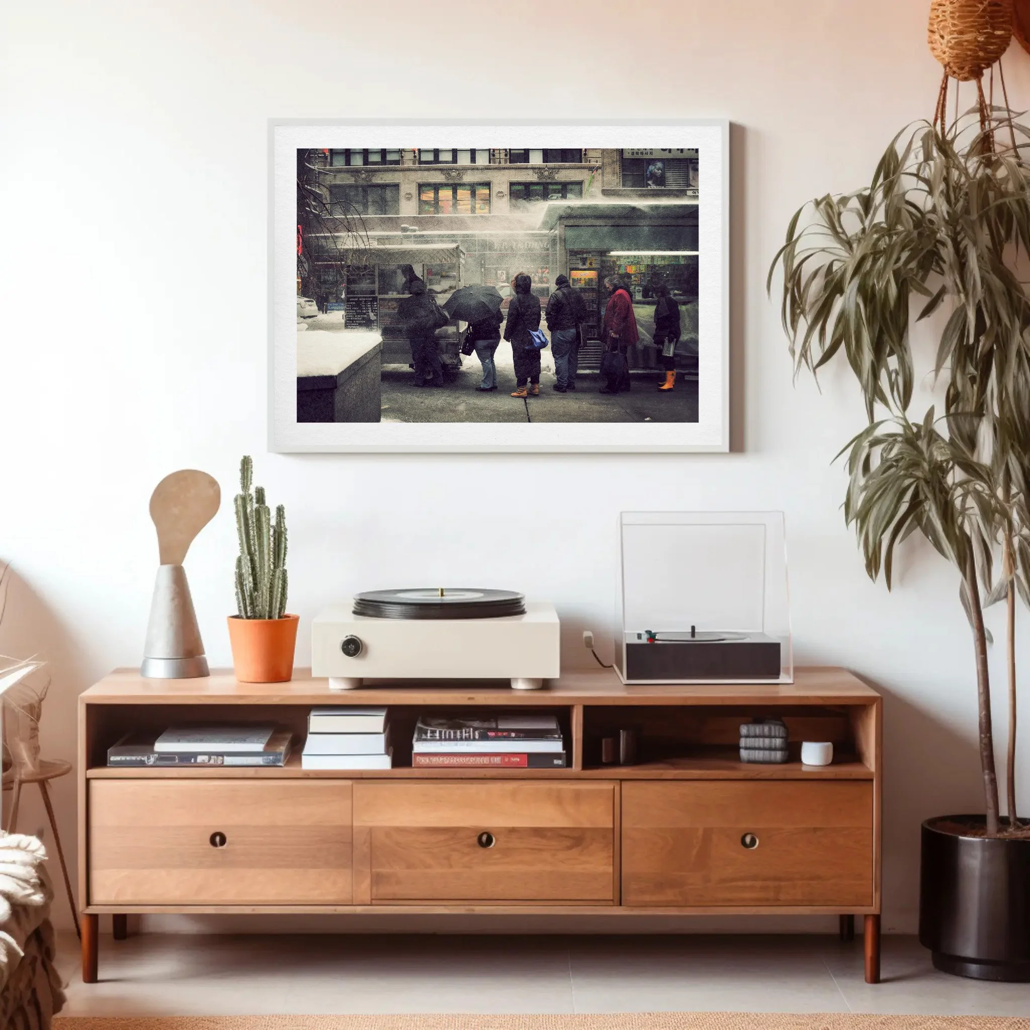 A wall-mounted framed photograph showing people waiting at a bus stop on a rainy day, reflected in a window with urban buildings behind.