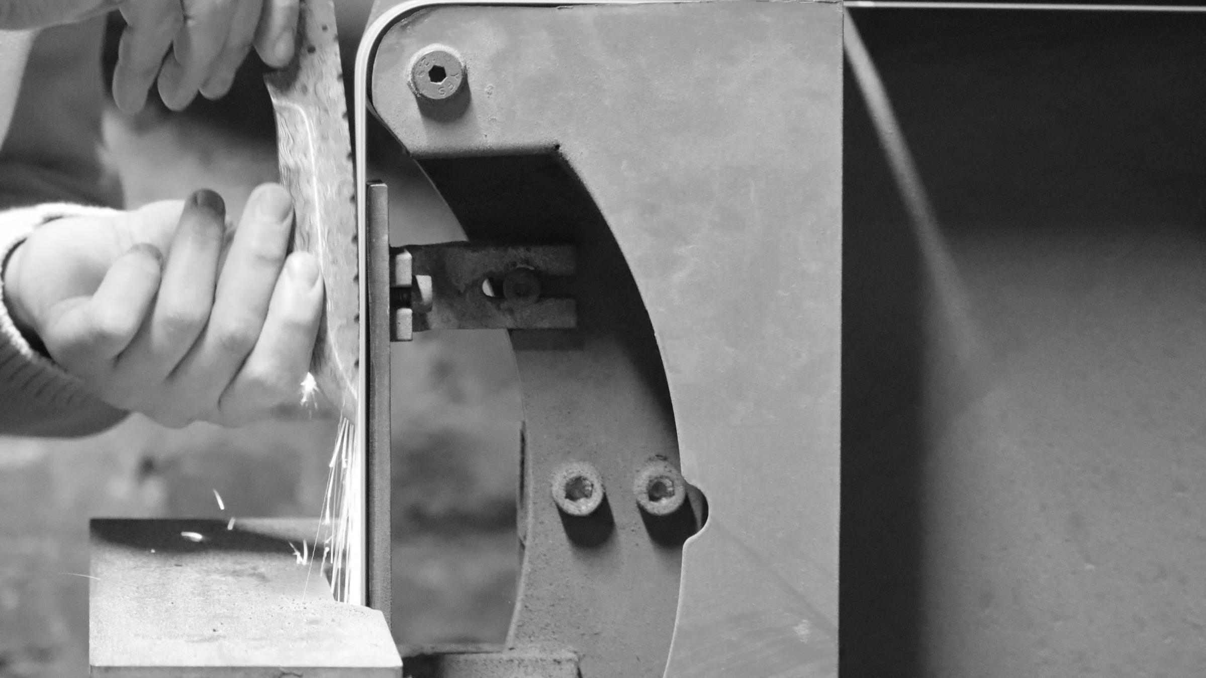 Black and white photo of a person welding metal on a workbench, with sparks flying from the welding process.
