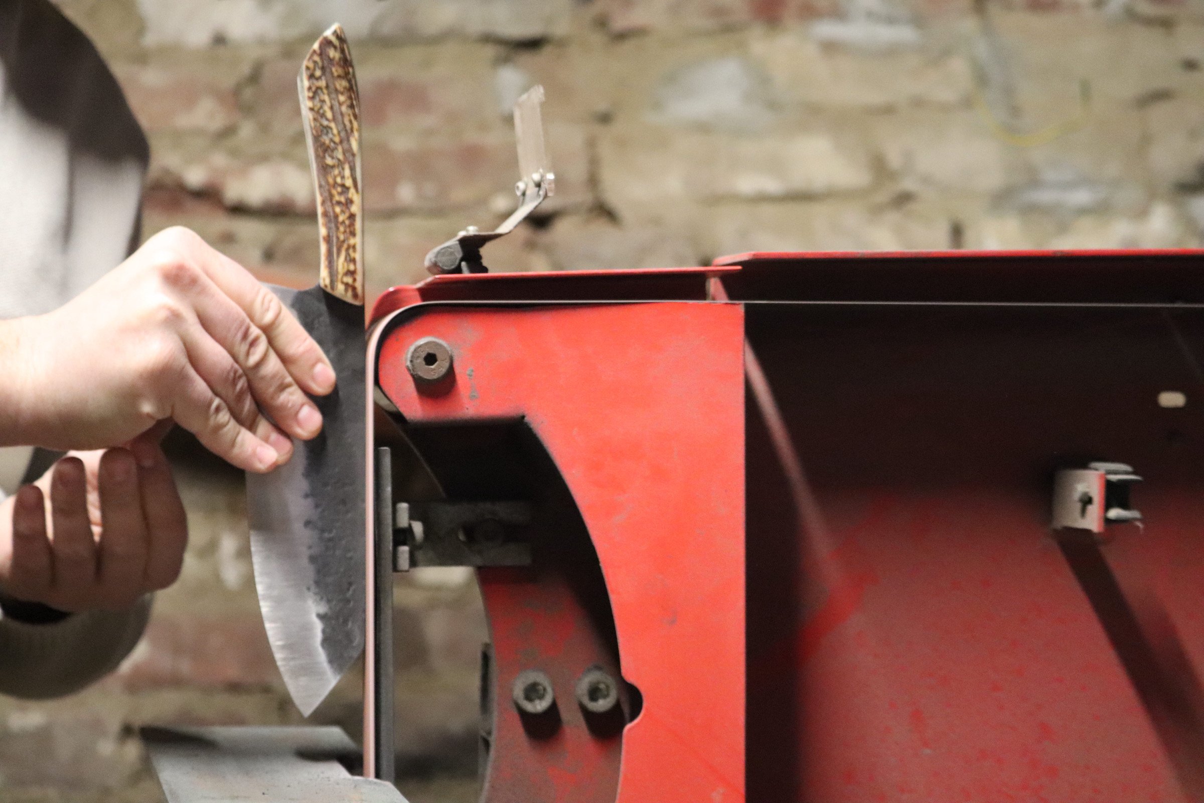 A close-up of a person assembling a red metal structure with a handsaw in a workshop with a brick wall in the background.