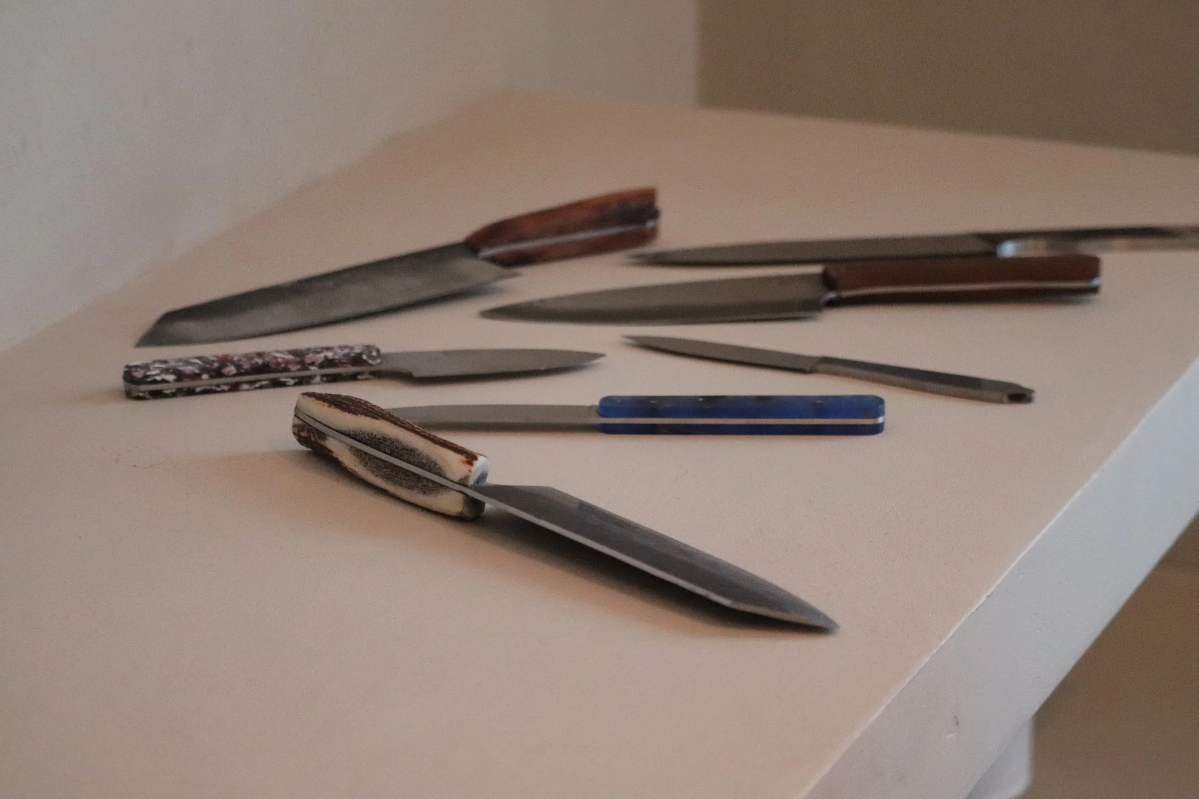 Collection of kitchen knives with various handle designs resting on a white surface.