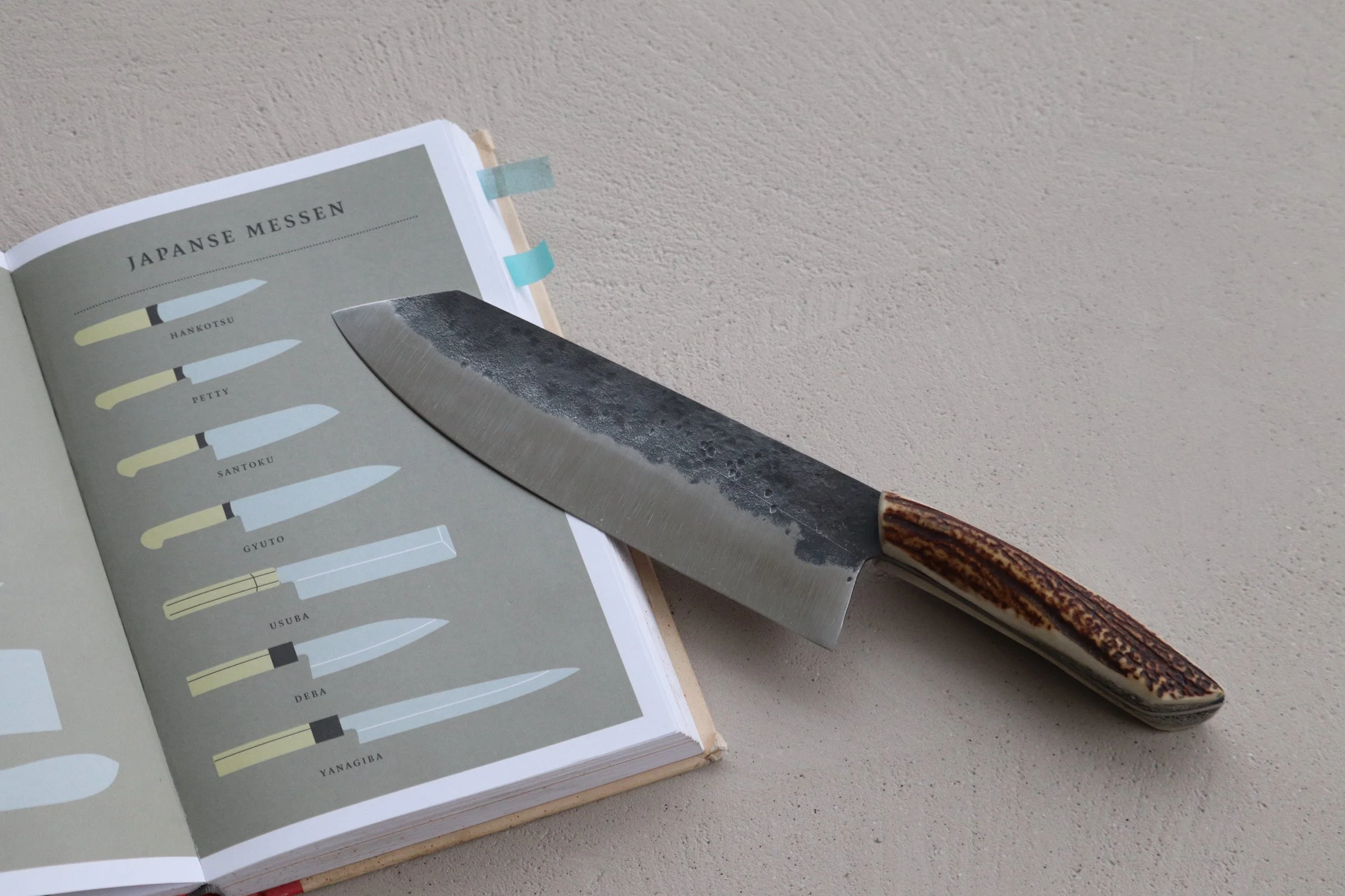 A Japanese kitchen knife resting on an open book about Japanese knives on a light-colored surface.