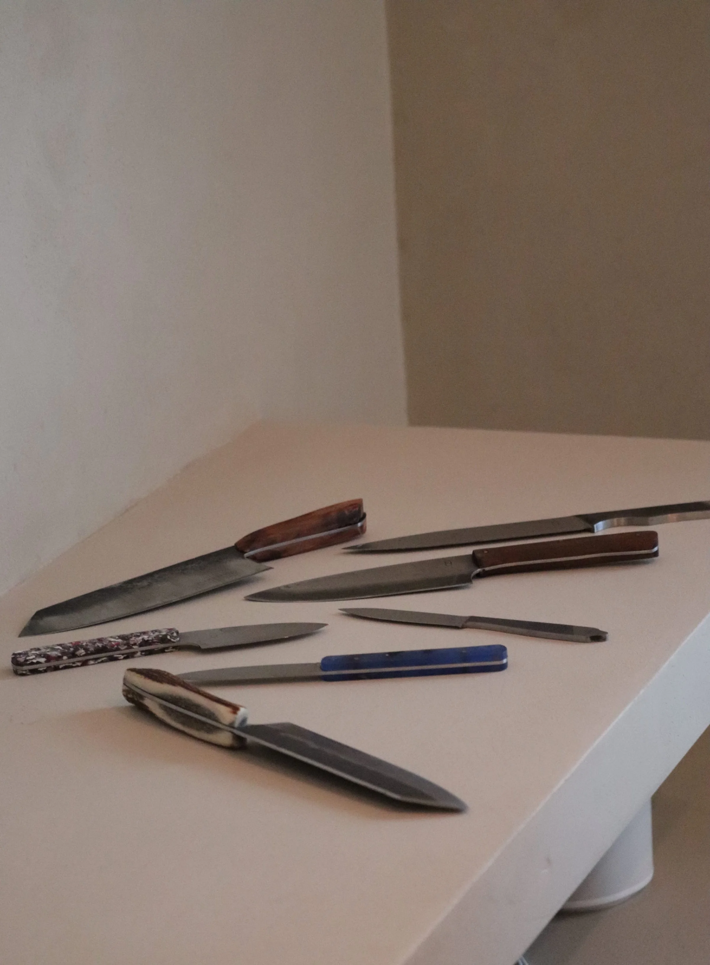 Collection of kitchen knives with various blade shapes and handles lying on a beige countertop.