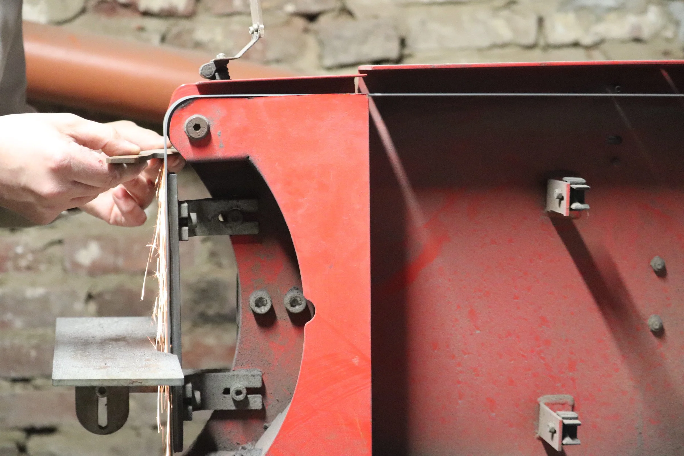 A person welding metal on a red industrial machine, sparks flying from the welding process, with a brick wall in the background.