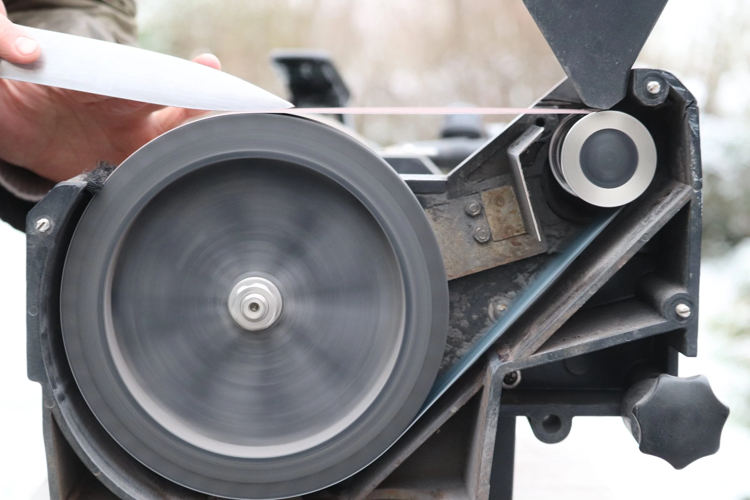 A close-up view of a circular saw blade rotating on a saw machine, with a person's hand holding a piece of material near the blade.