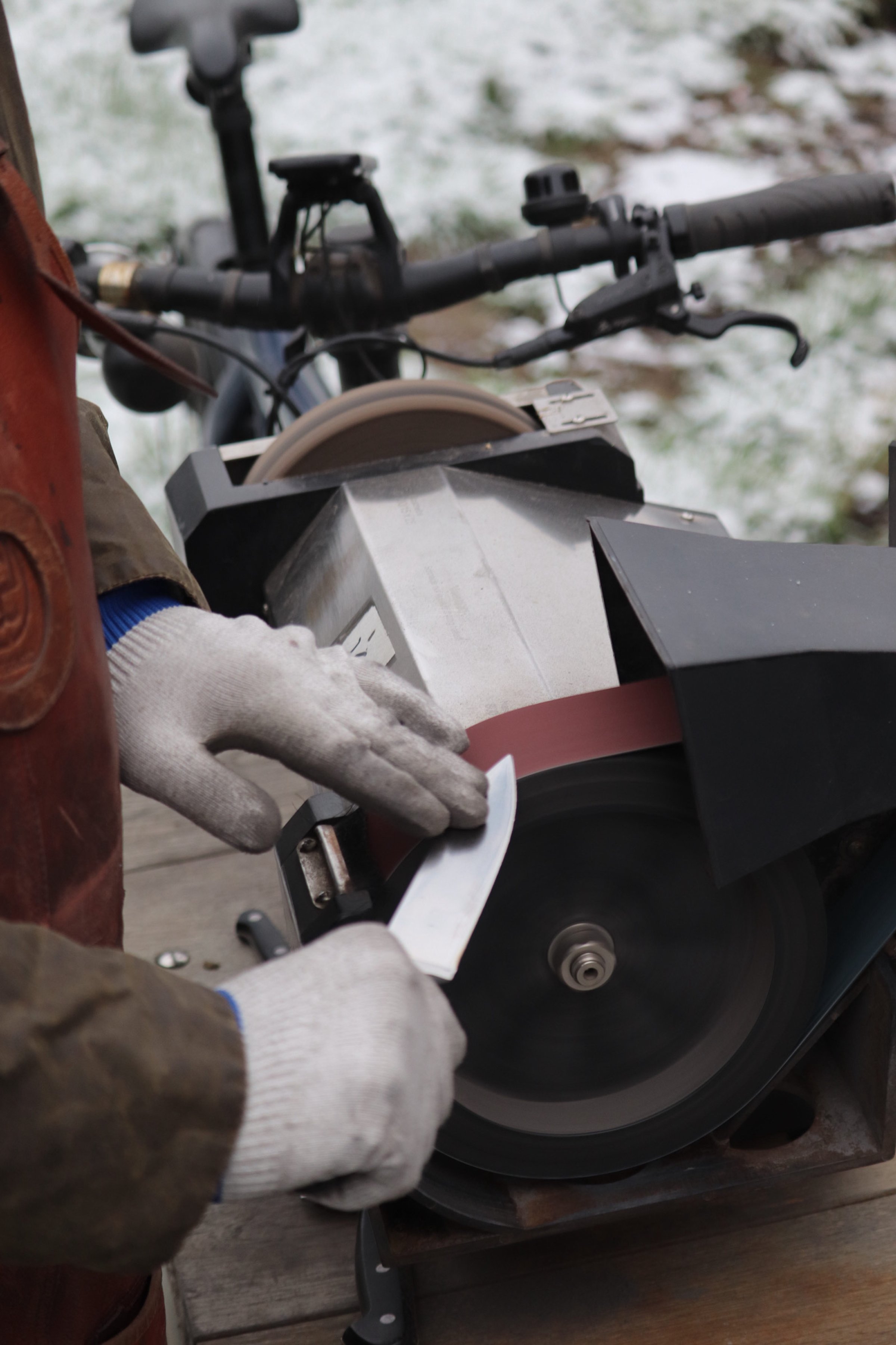 Person using a small handheld tool to smooth a strip of abrasive material on a circular saw blade outside in a winter setting.