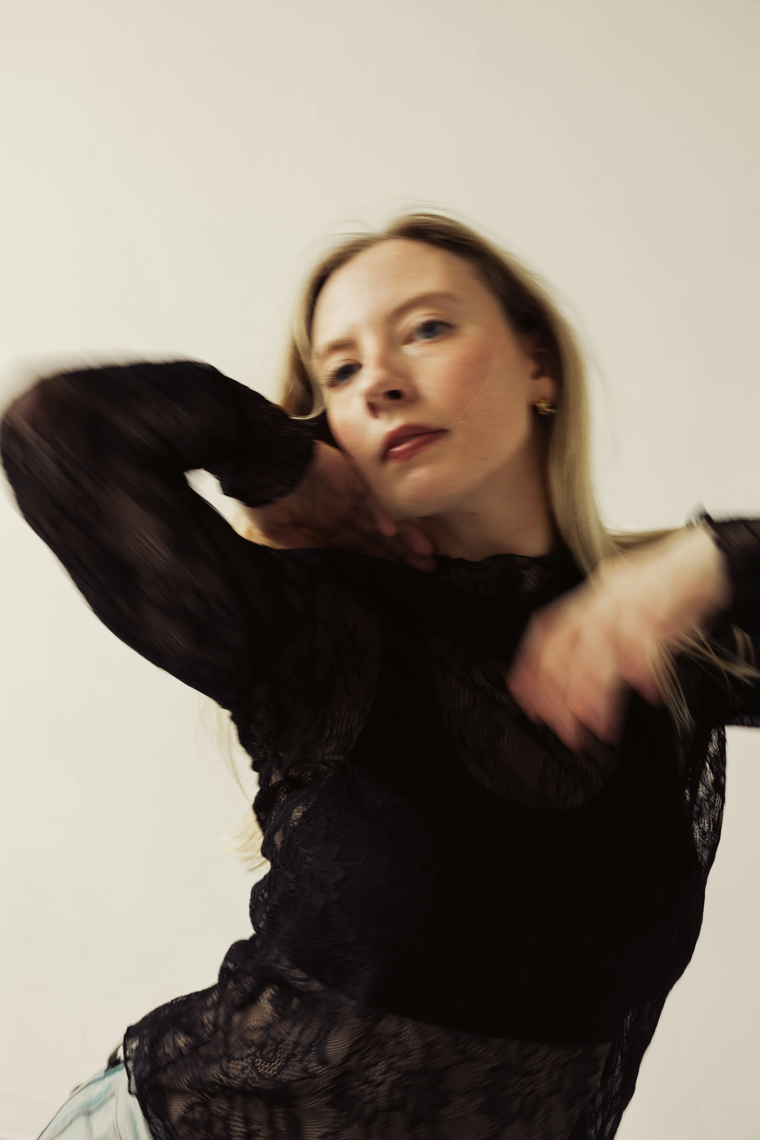 A woman with blonde hair and light skin wearing a black lace top poses against a plain background.