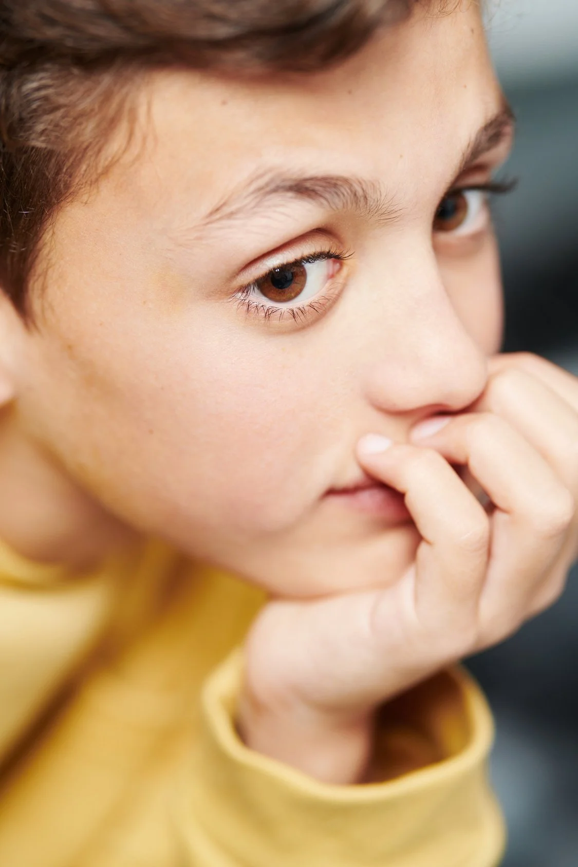 Jeune garçon avec teint clair, yeux marron, habillé en jaune, posant avec main près du visage.