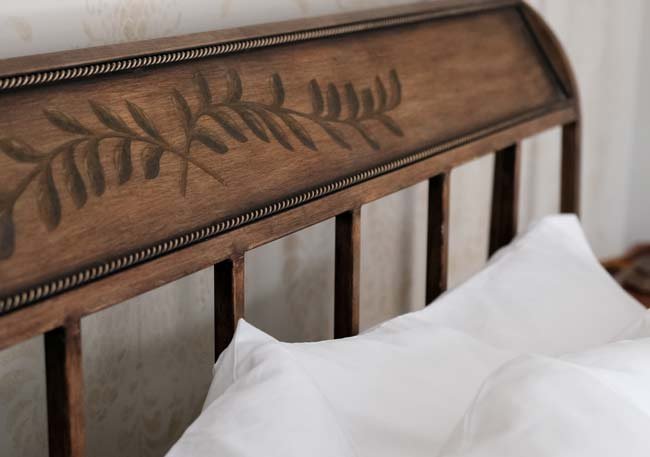 Close-up of a wooden headboard with carved leaf design, partially visible white pillows and bed linens.