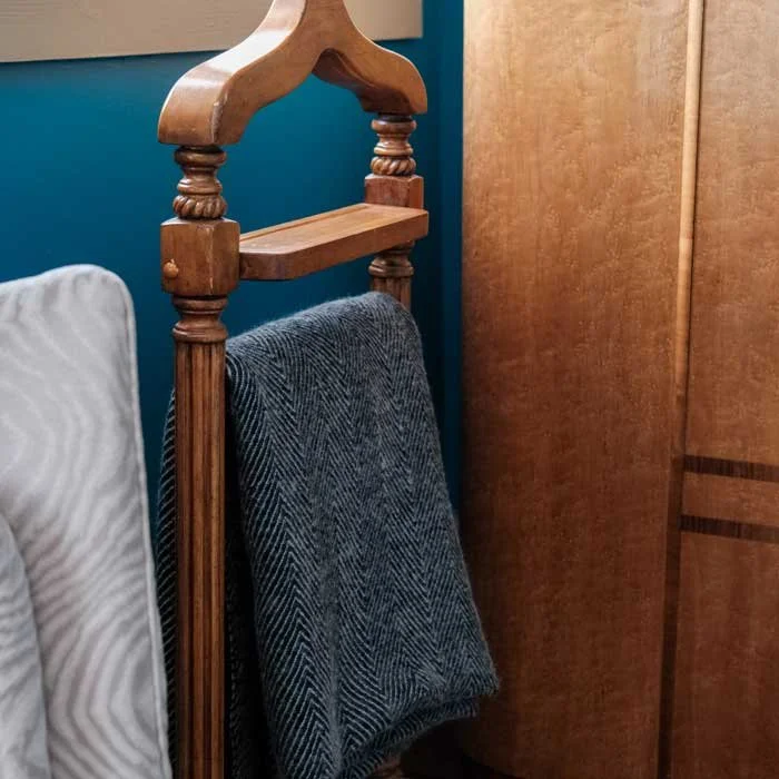 A wooden coat rack with a blanket hanging on it, next to a wardrobe and a wall with a teal paint color.