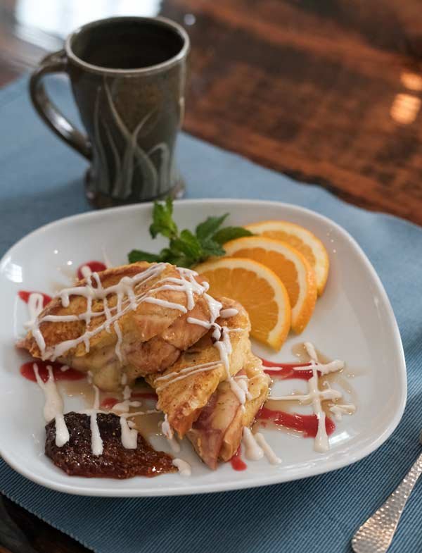 Fried chicken with white sauce on a white plate, garnished with orange slices and a sprig of parsley, with a cup of black coffee in the background.