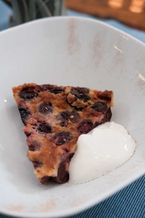 A slice of blueberry pie with a dollop of whipped cream in a white bowl.