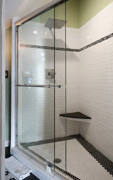Empty walk-in shower with glass doors, white subway tile walls, black tile accents, a built-in corner seat, and a rainfall showerhead.