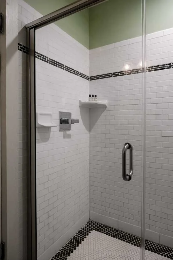 A tiled shower with white subway tiles, a black mosaic tile border, and a black and white hexagonal tile floor.