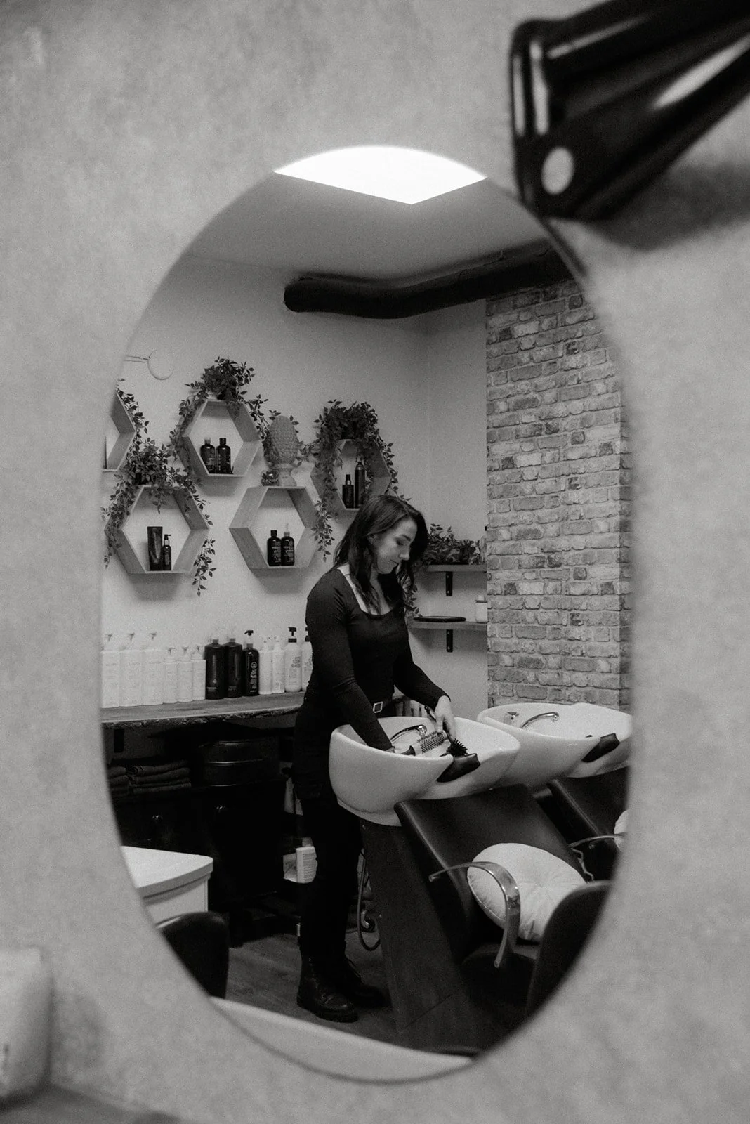 Mustavalkoinen yrityskuva peilin kautta otettuna, kampaaja pesupisteellä.