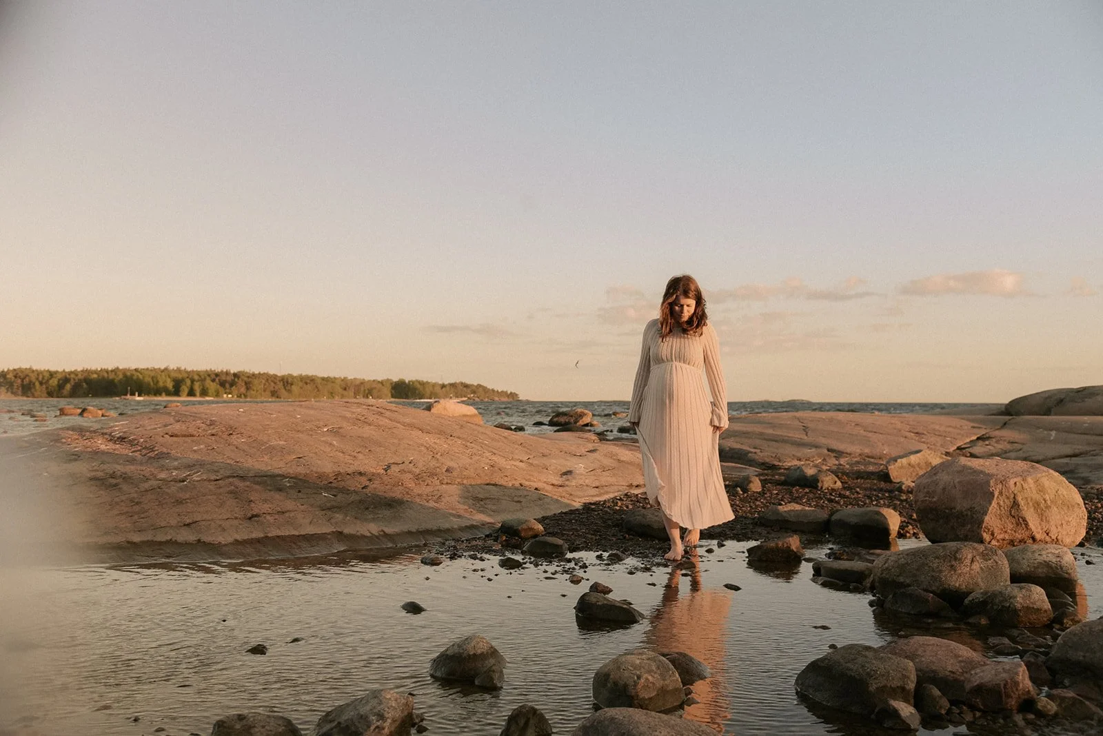 Kalliolla kävelevä odottava äiti ilta-auringossa. Raskauskuvaus Helsinki.