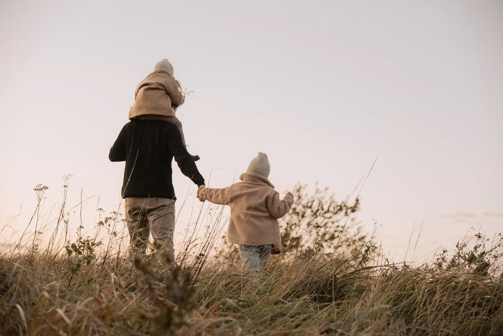 Perhekuvaus miljöössä, isä kantaa lasta olkapäillä ja pitää toista kädestä. Kuvannut valokuvaaja Heidi Väisänen.