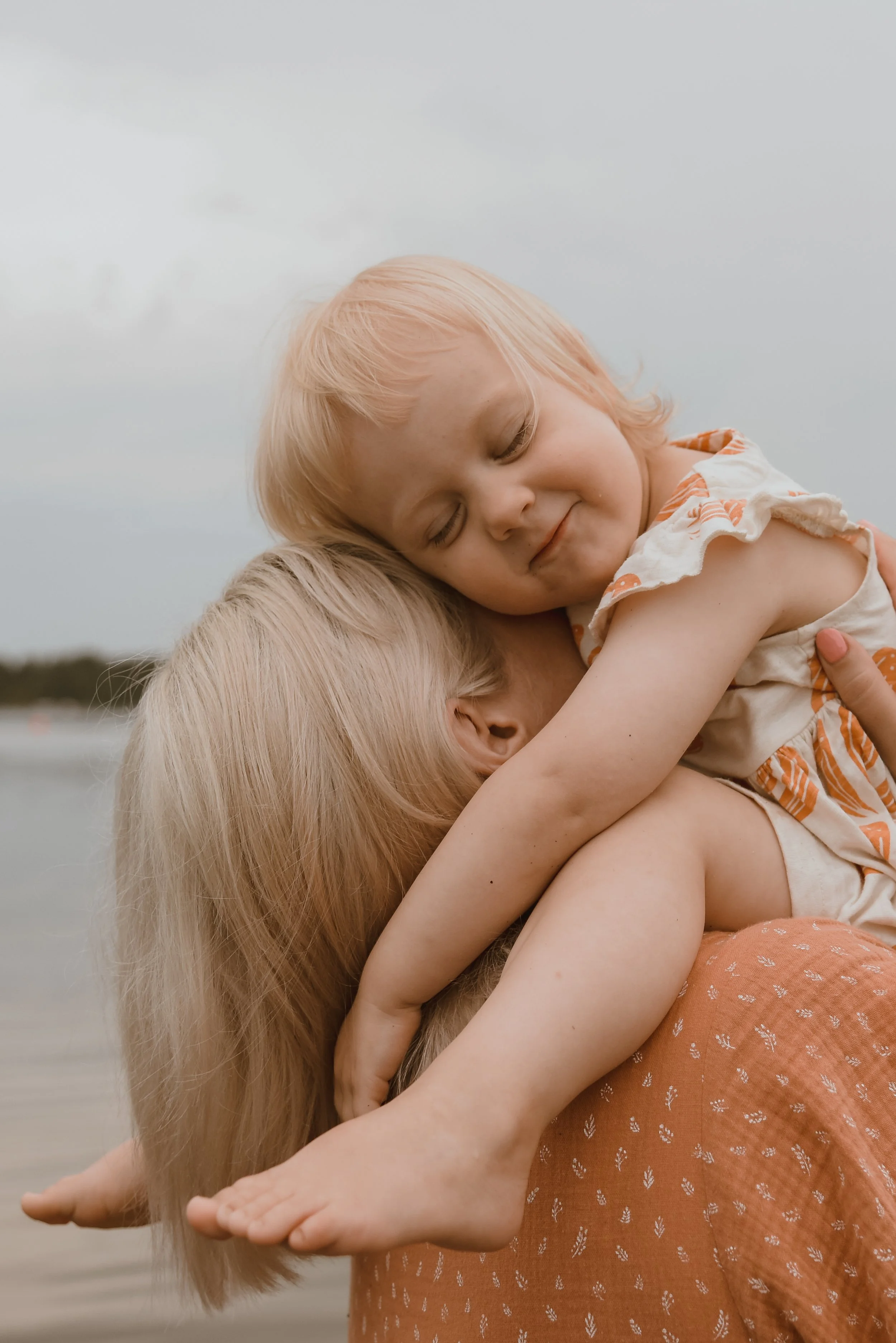 Valokuvaus ulkona, perhekuva, jossa lapsi istuu äidin olkapäillä ja halaa äitiä.