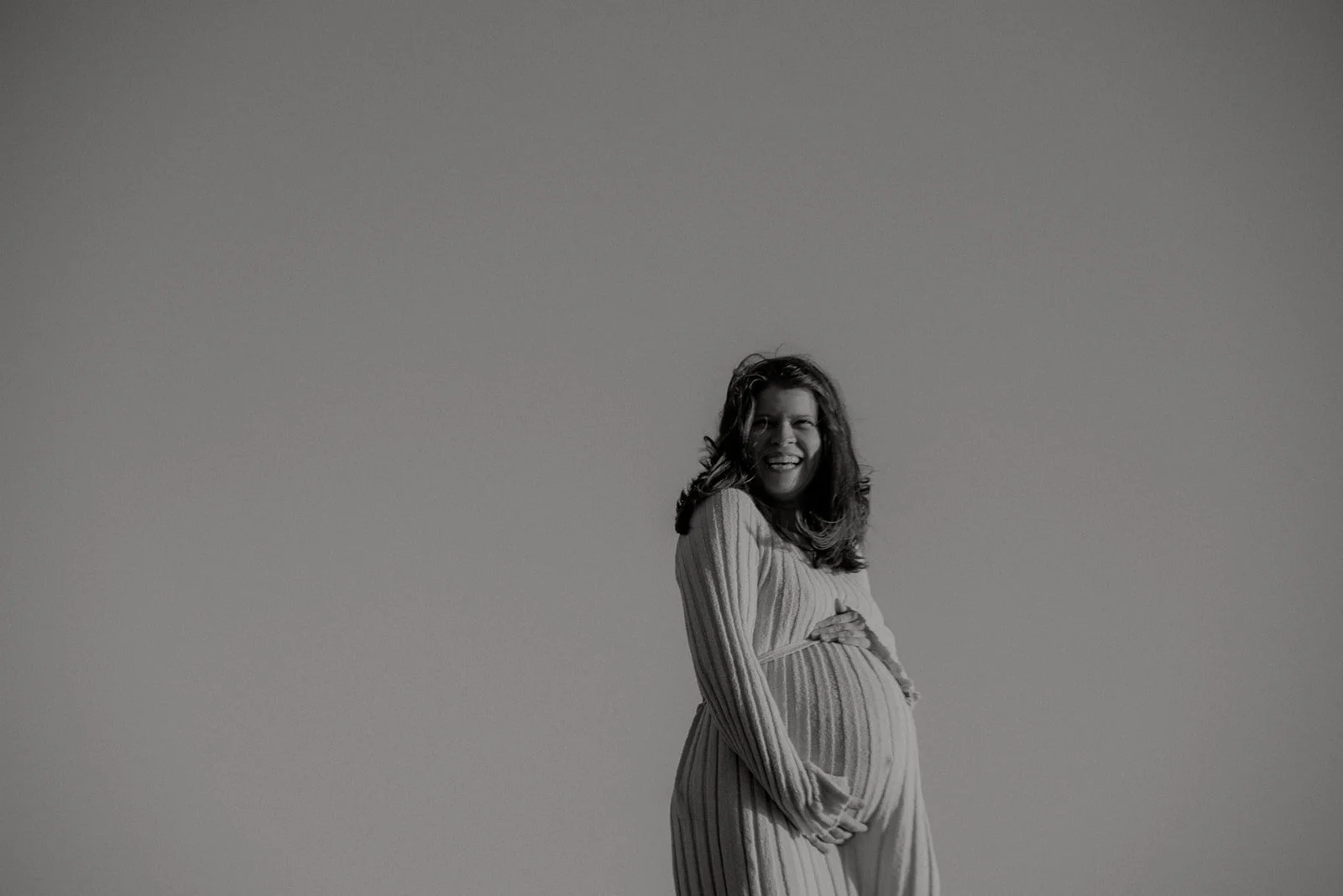 Raskaana oleva nainen pitelee vatsaansa mustavalkokuvassa. Odotusajankuvaus Espoo.
